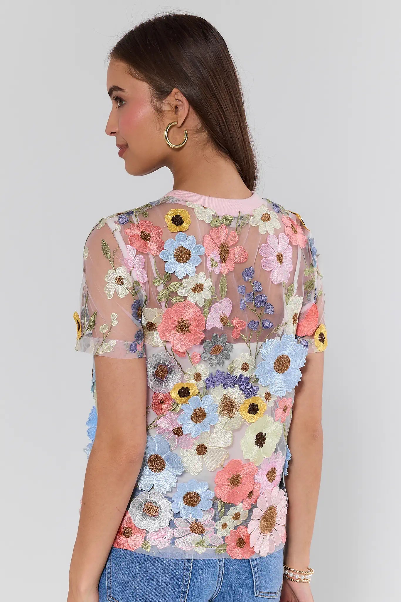 Woman wearing a floral mesh top with a plain background