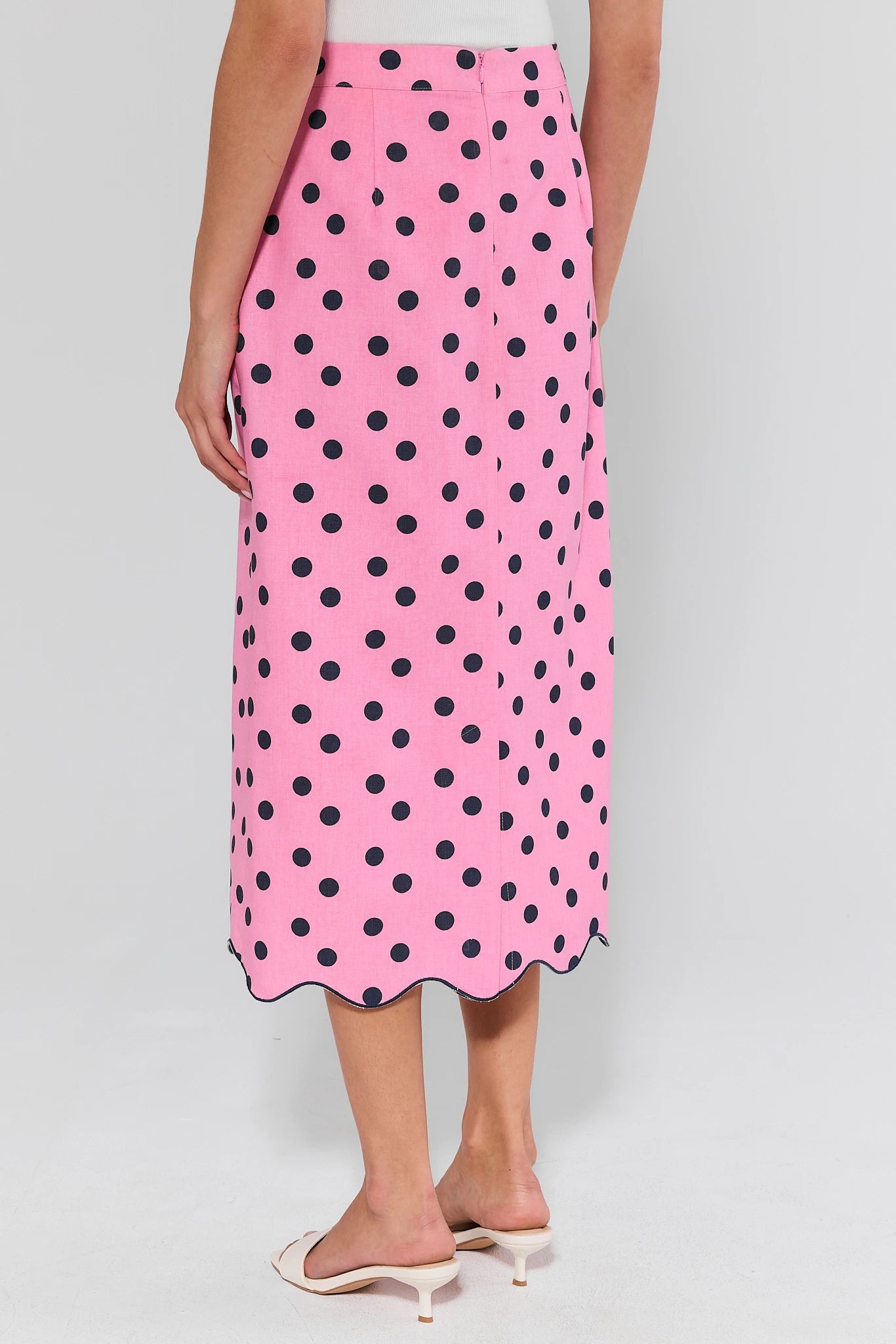 Pink skirt with black polka dots worn by a person on a white background
