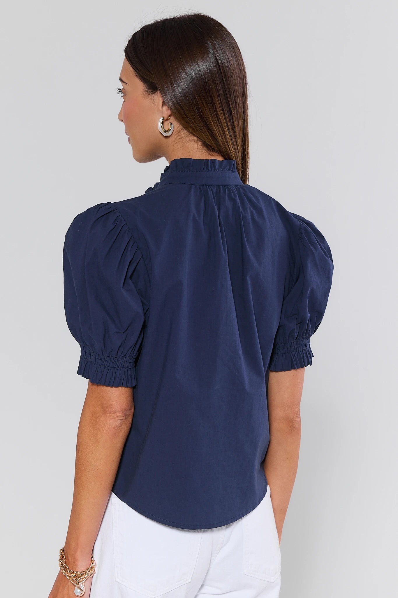 Woman wearing a navy blue blouse with puffed sleeves on a light gray background