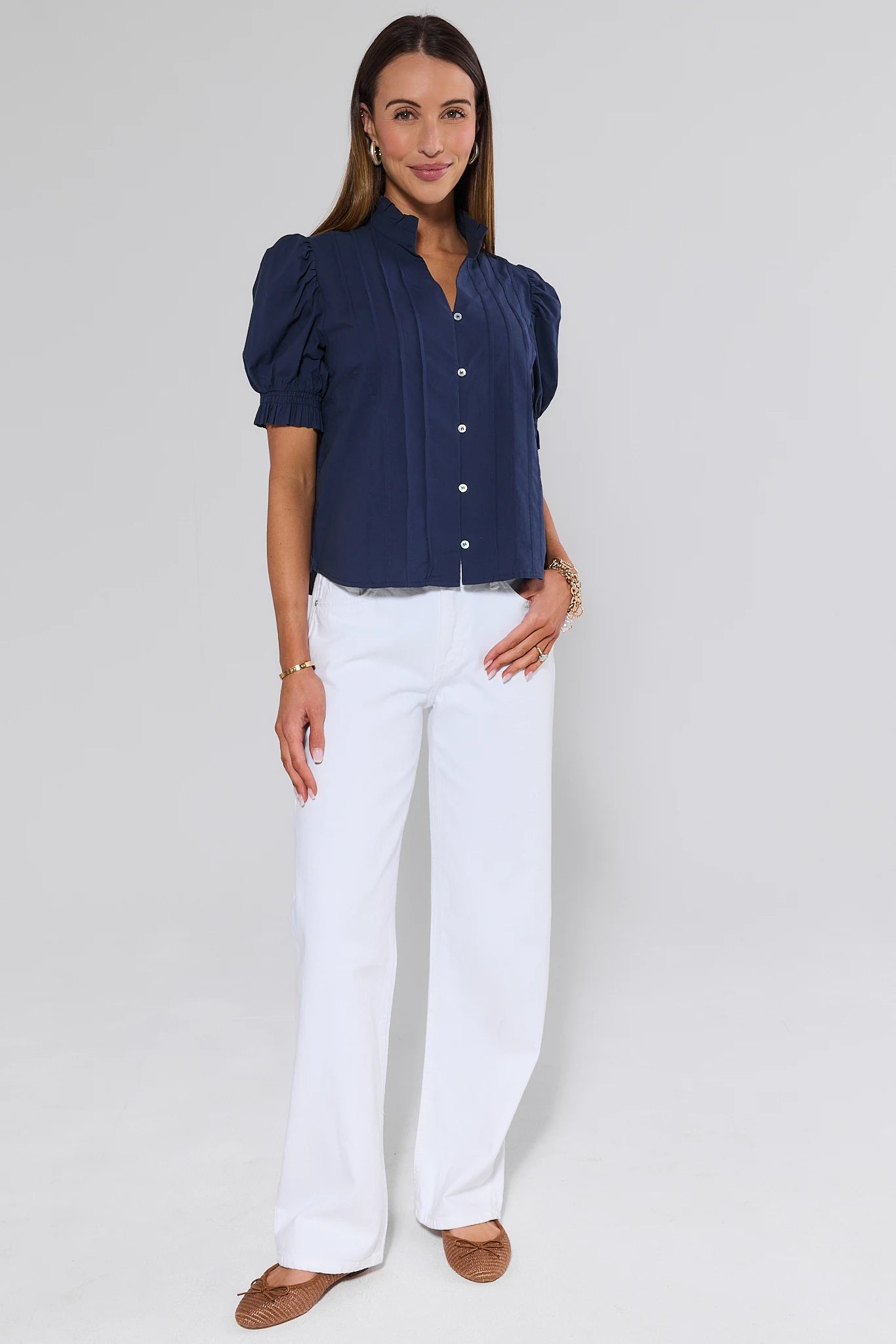 Woman wearing a navy blue blouse and white pants on a plain background