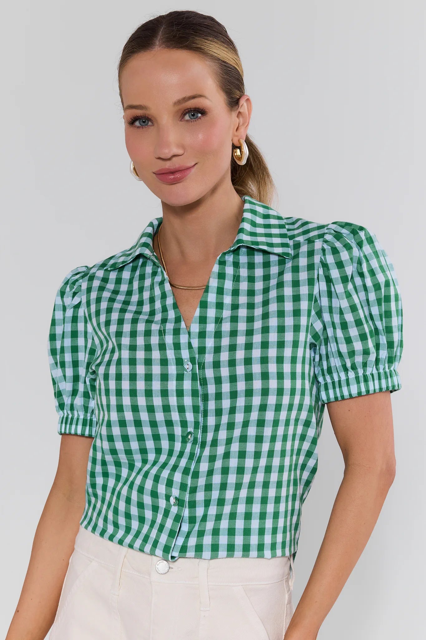 Woman wearing a green and white checkered blouse against a plain background