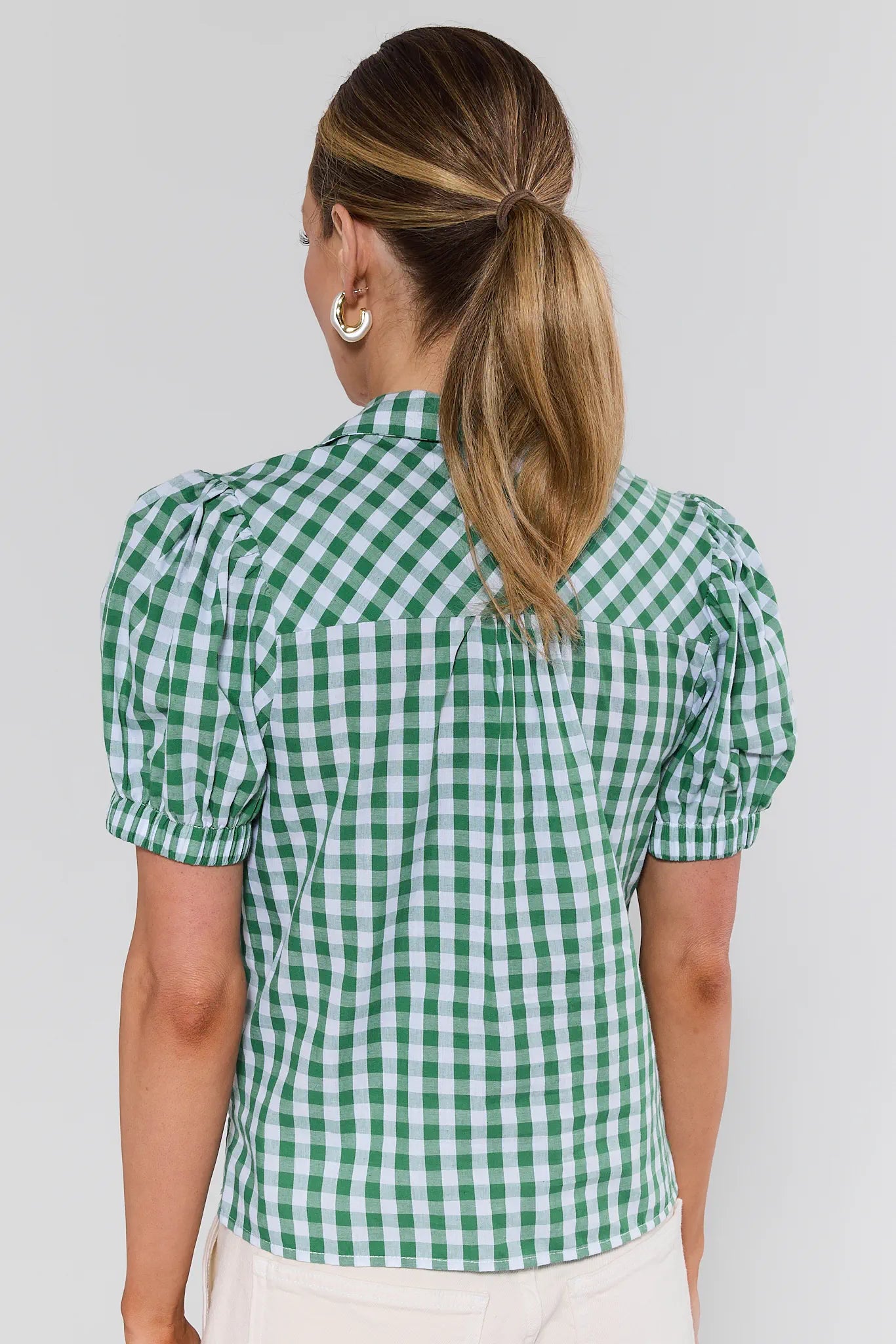 Woman wearing a green and white checkered blouse against a plain background