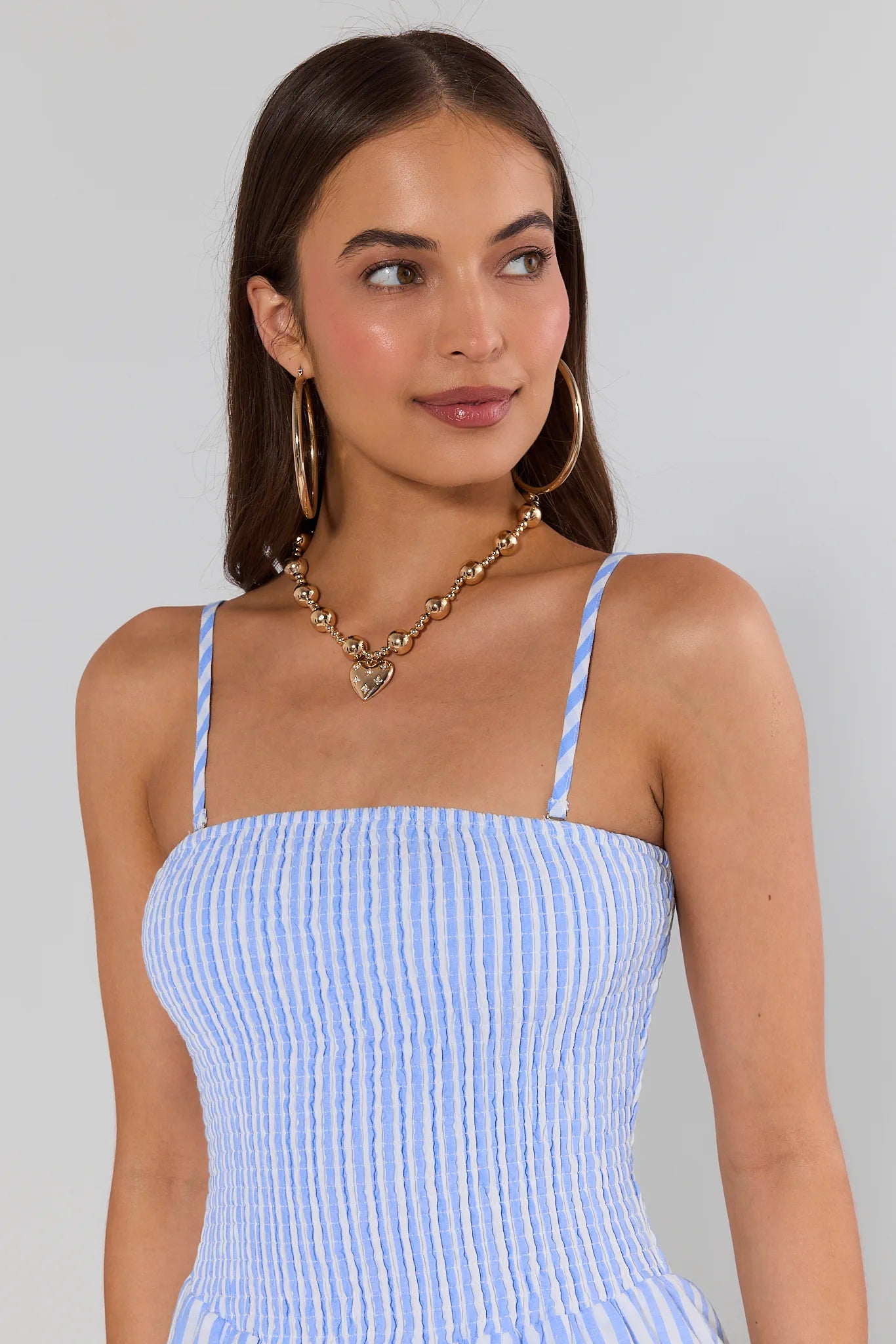 Woman wearing a blue and white striped dress with gold jewelry against a gray background