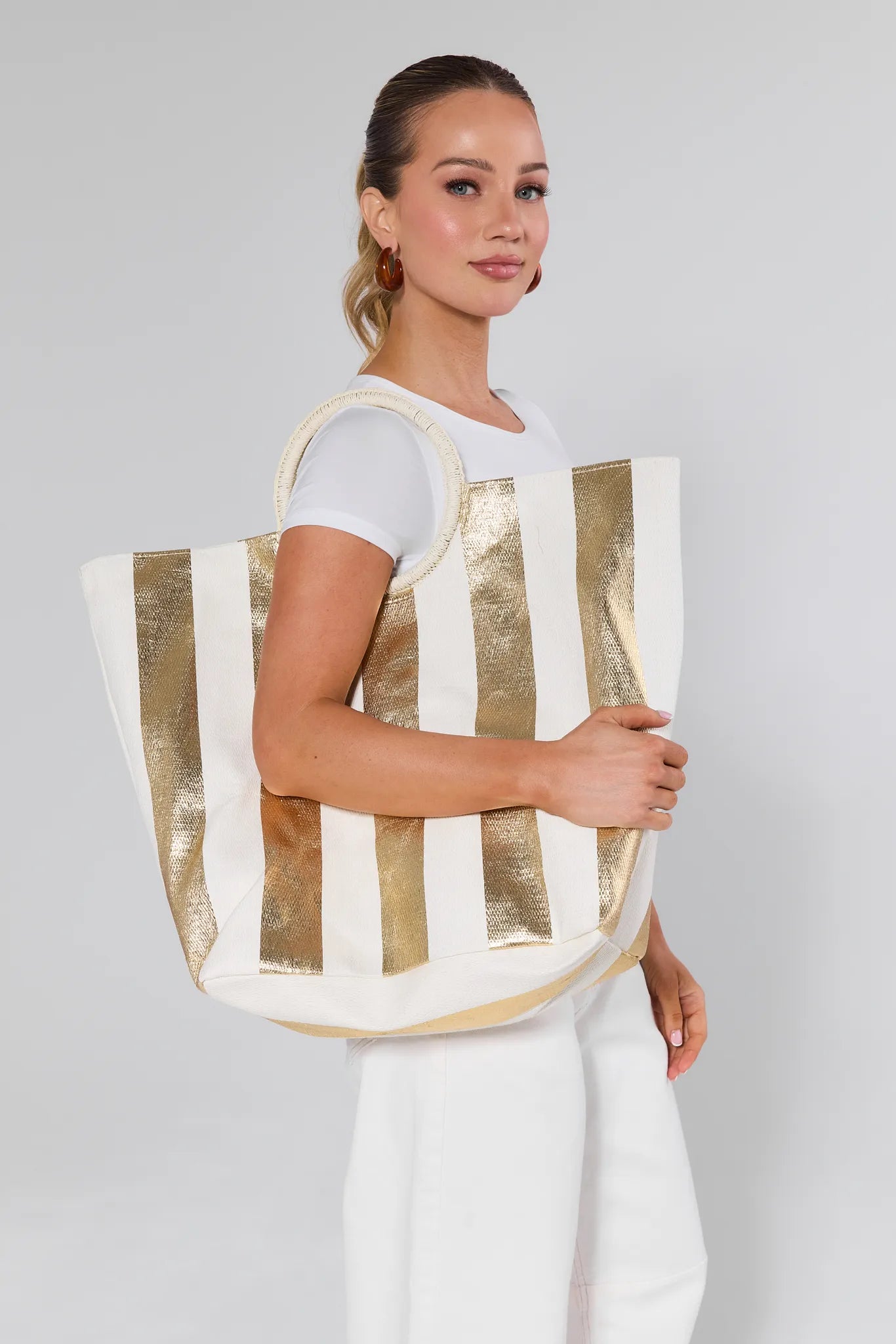 Woman holding a large Maurice Tote with gold and white stripes against a plain background