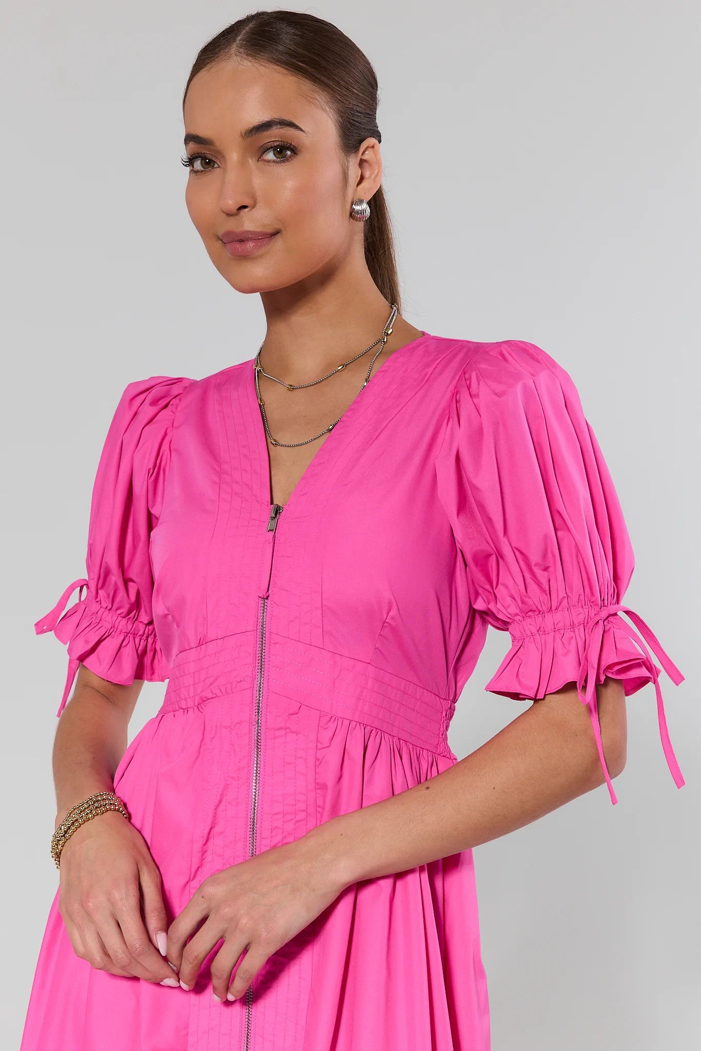CLOSE UP Woman wearing a bright pink dress with puffed sleeves against a plain background