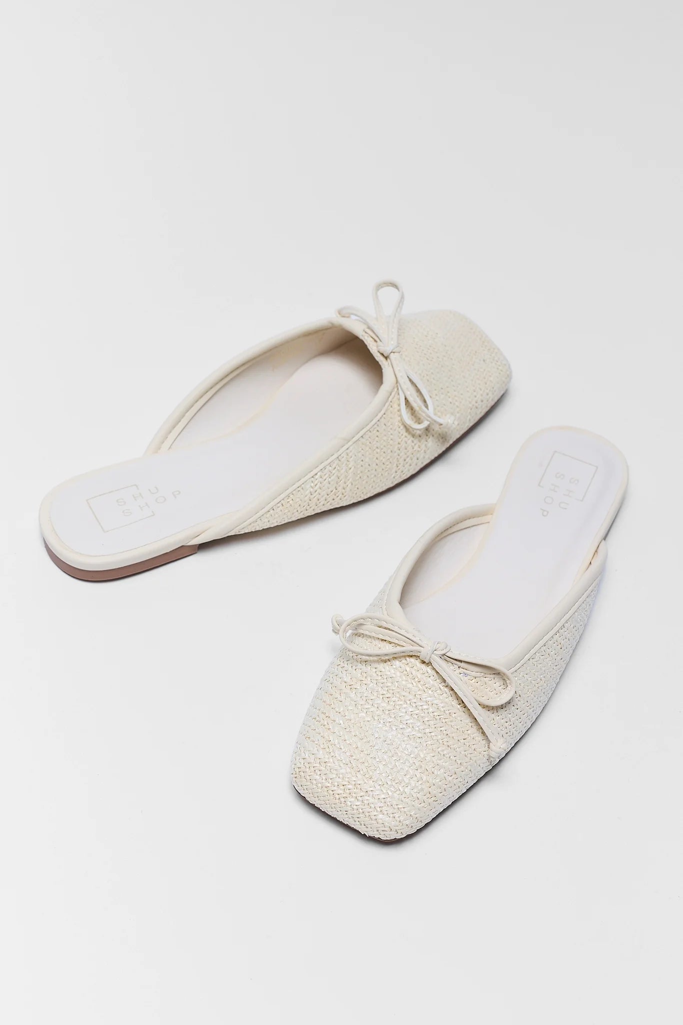 Pair of cream-colored slippers with bow details on a light gray background