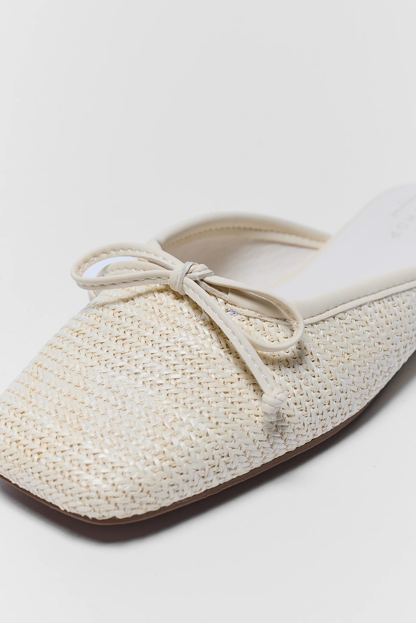 White woven flat shoe with a bow on a light background