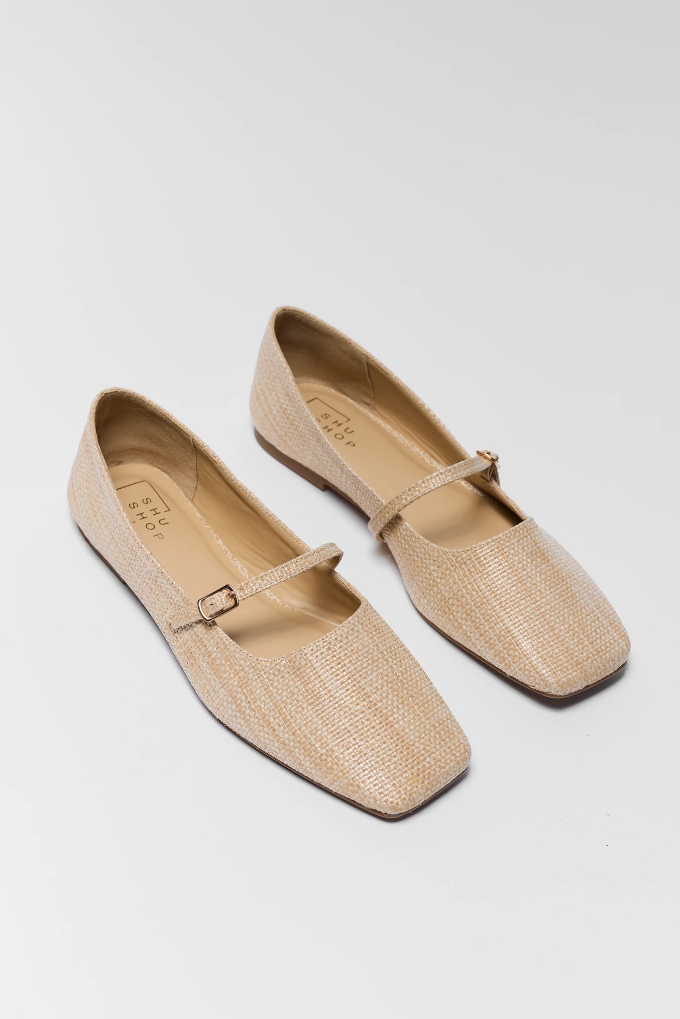 Pair of beige loafers with a strap on a light gray background