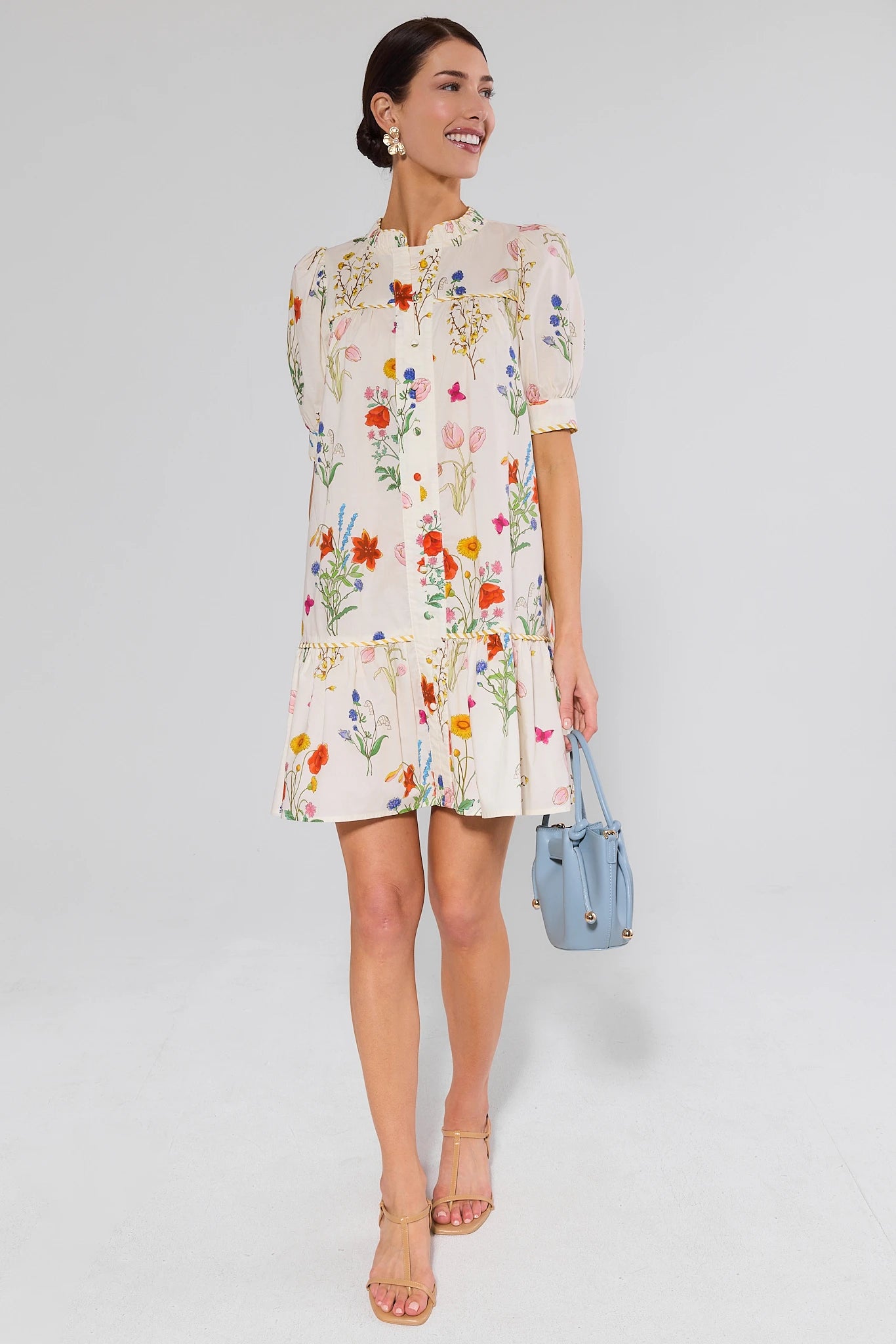 Woman wearing a floral dress holding a blue handbag on a white background
