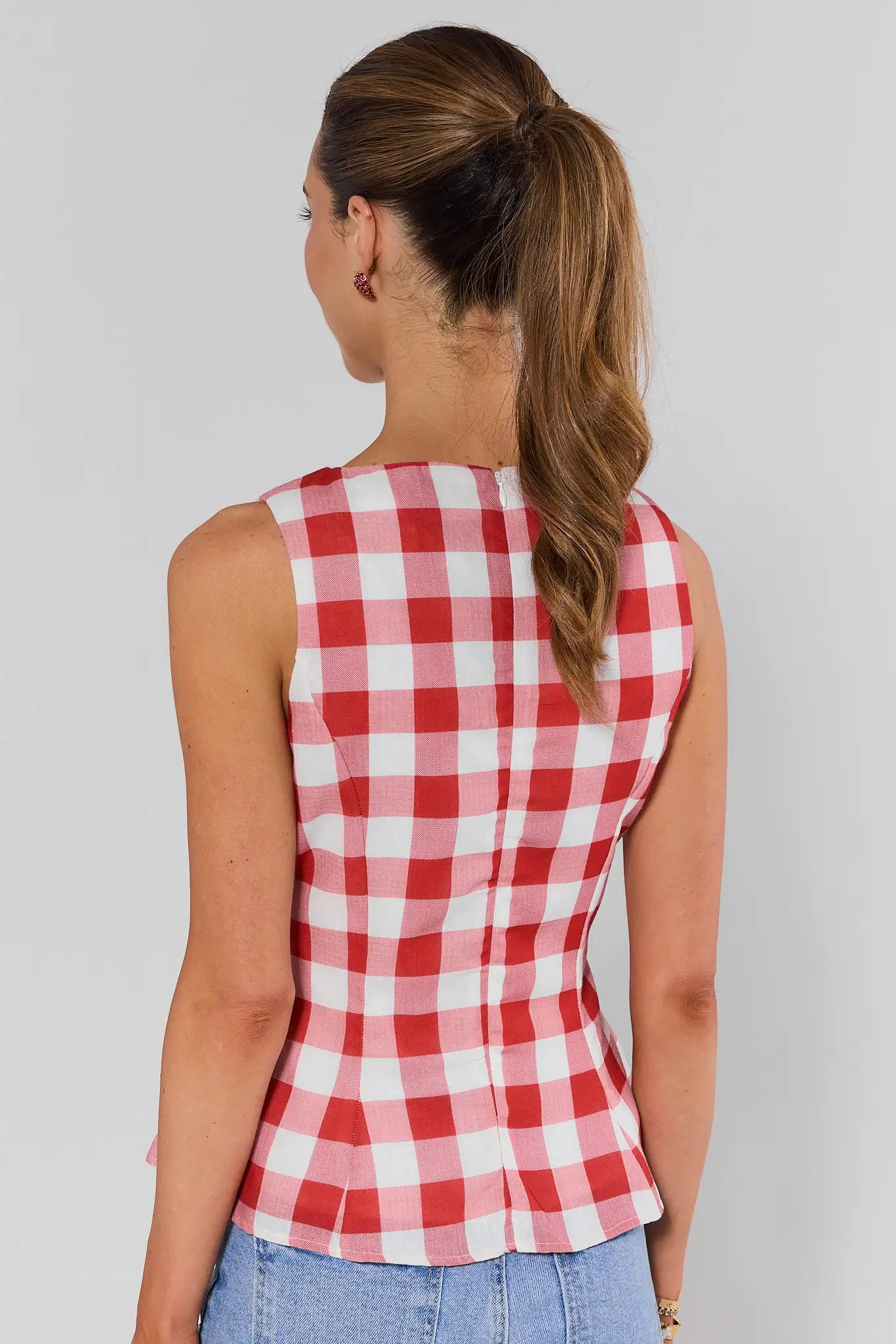 Woman standing wearing a red and white checkered sleeveless top against a plain background