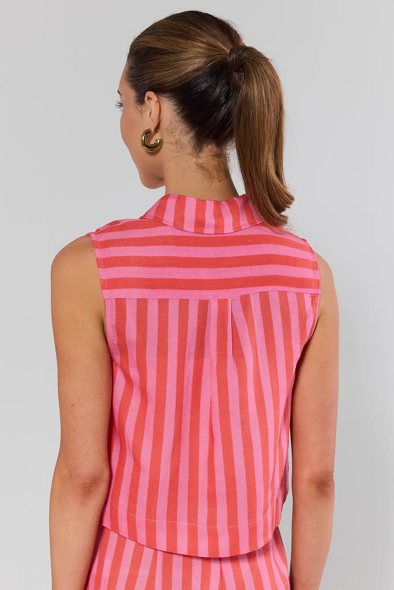 Woman standing wearing a sleeveless pink and white striped shirt against a plain background