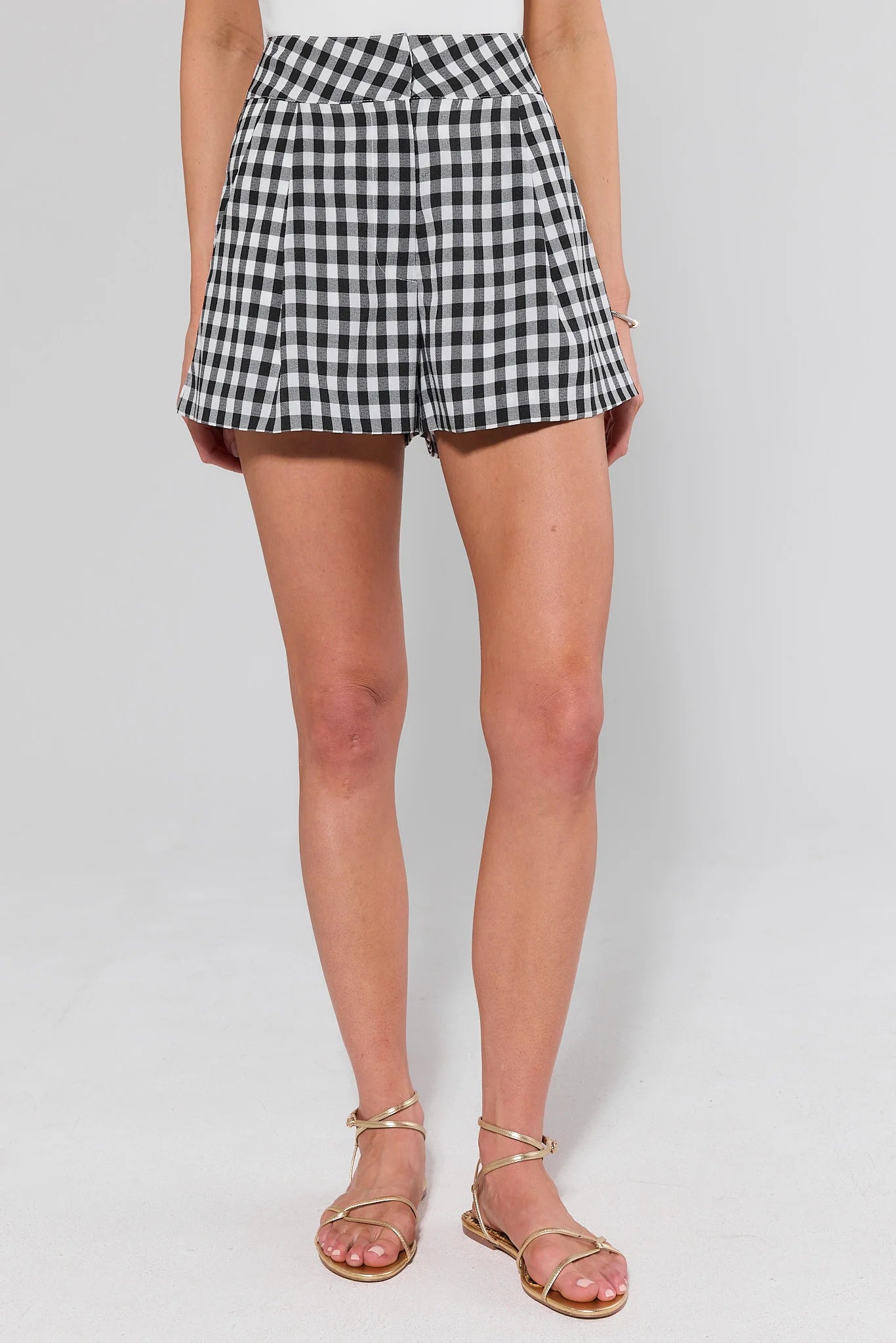 Person wearing black and white checkered shorts and gold sandals on a plain background