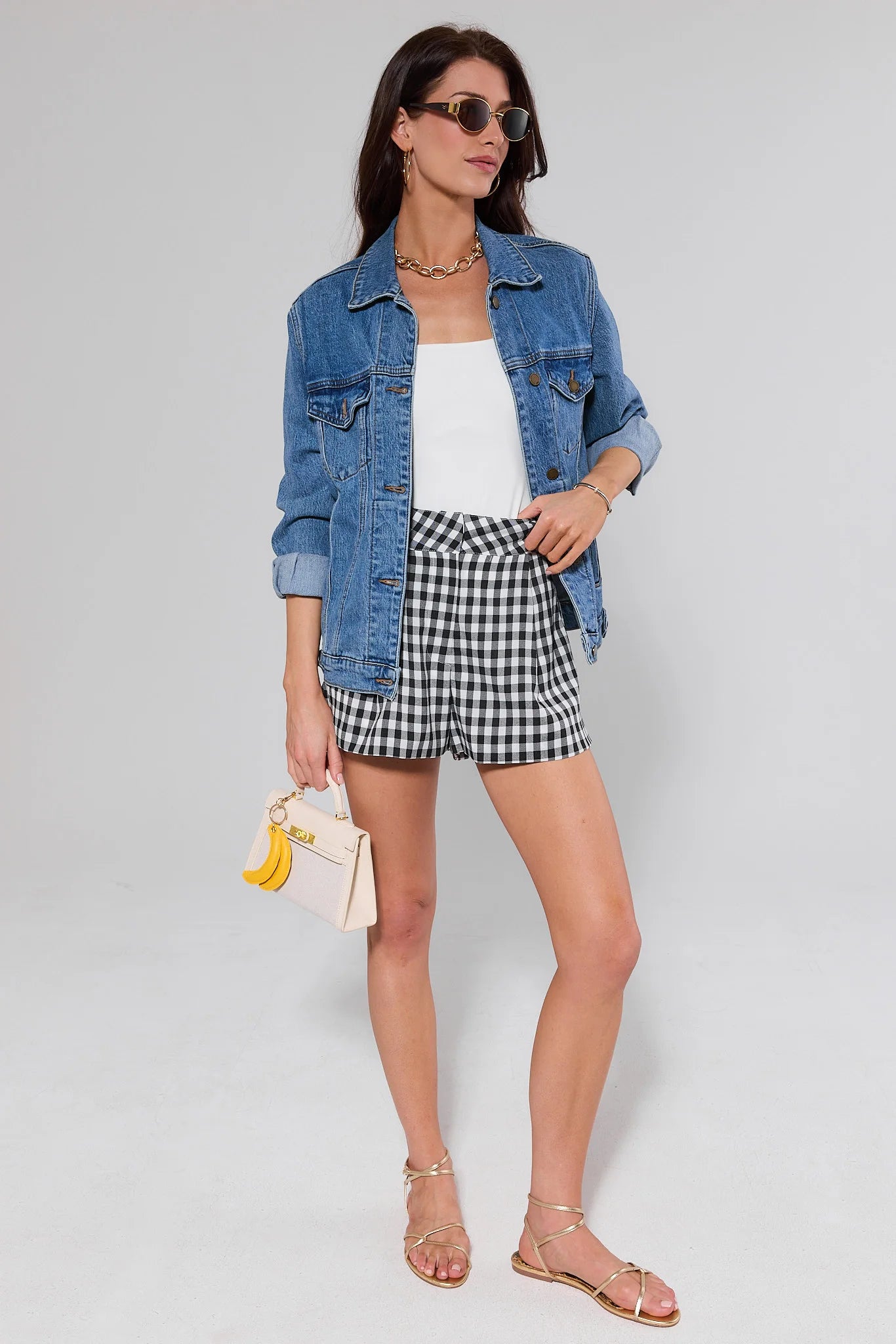 Woman wearing a denim jacket, white top, and checkered shorts on a plain background
