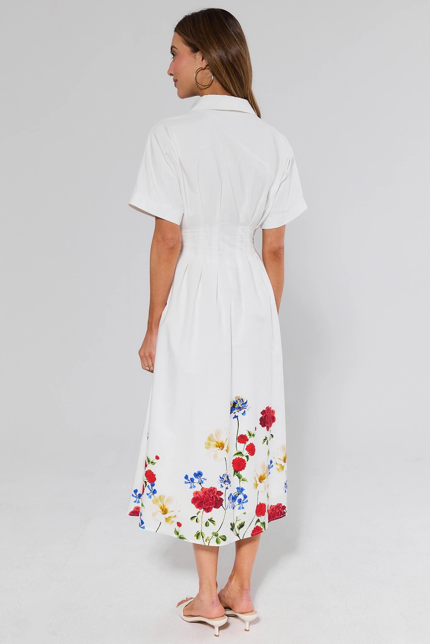Woman standing wearing a white dress with colorful floral embroidery on a plain background