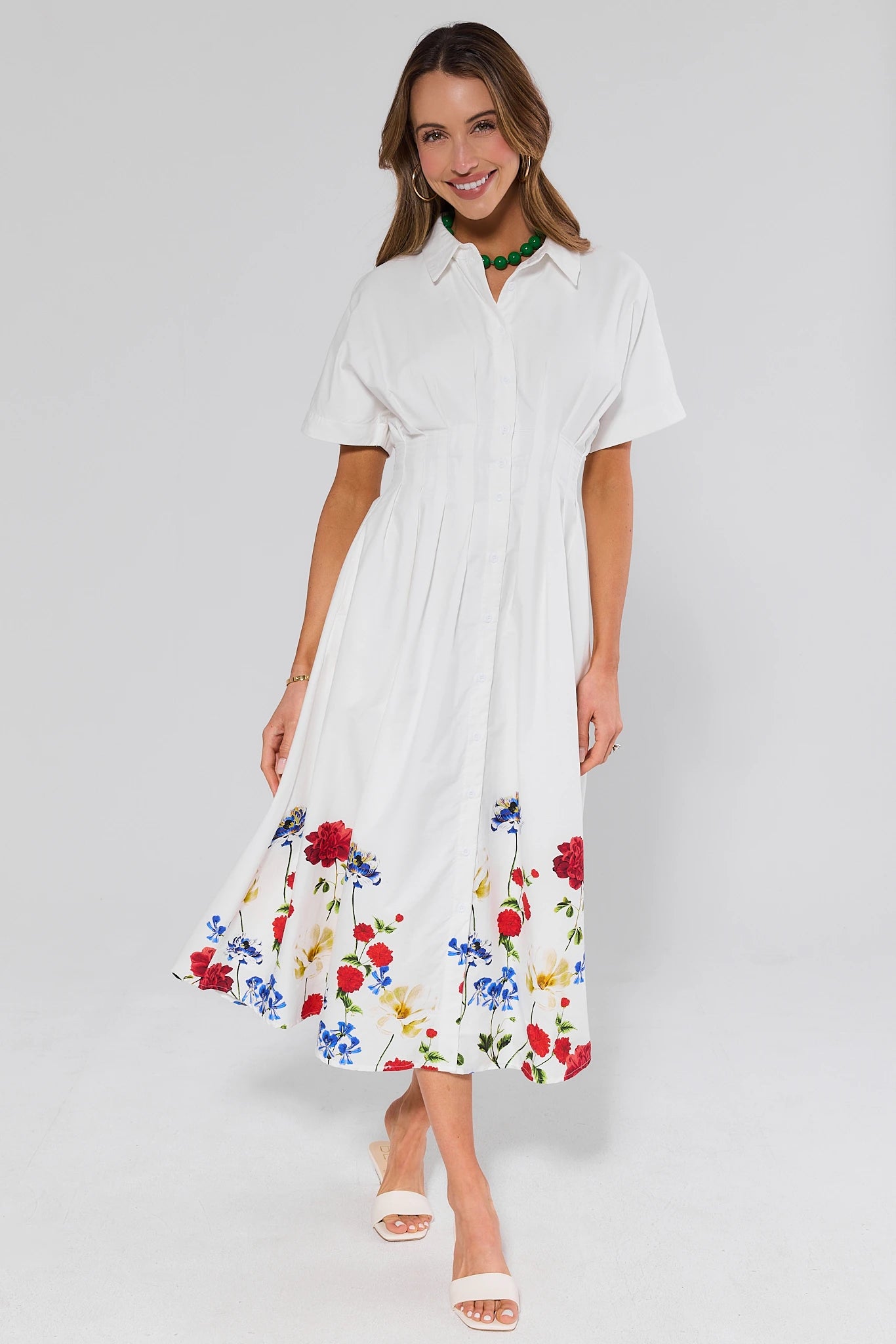 Woman wearing a white dress with floral patterns and white heels on a plain background