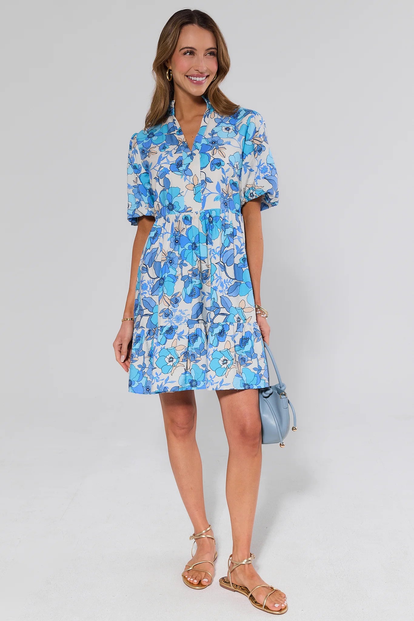 Woman wearing a blue floral dress with sandals against a plain background