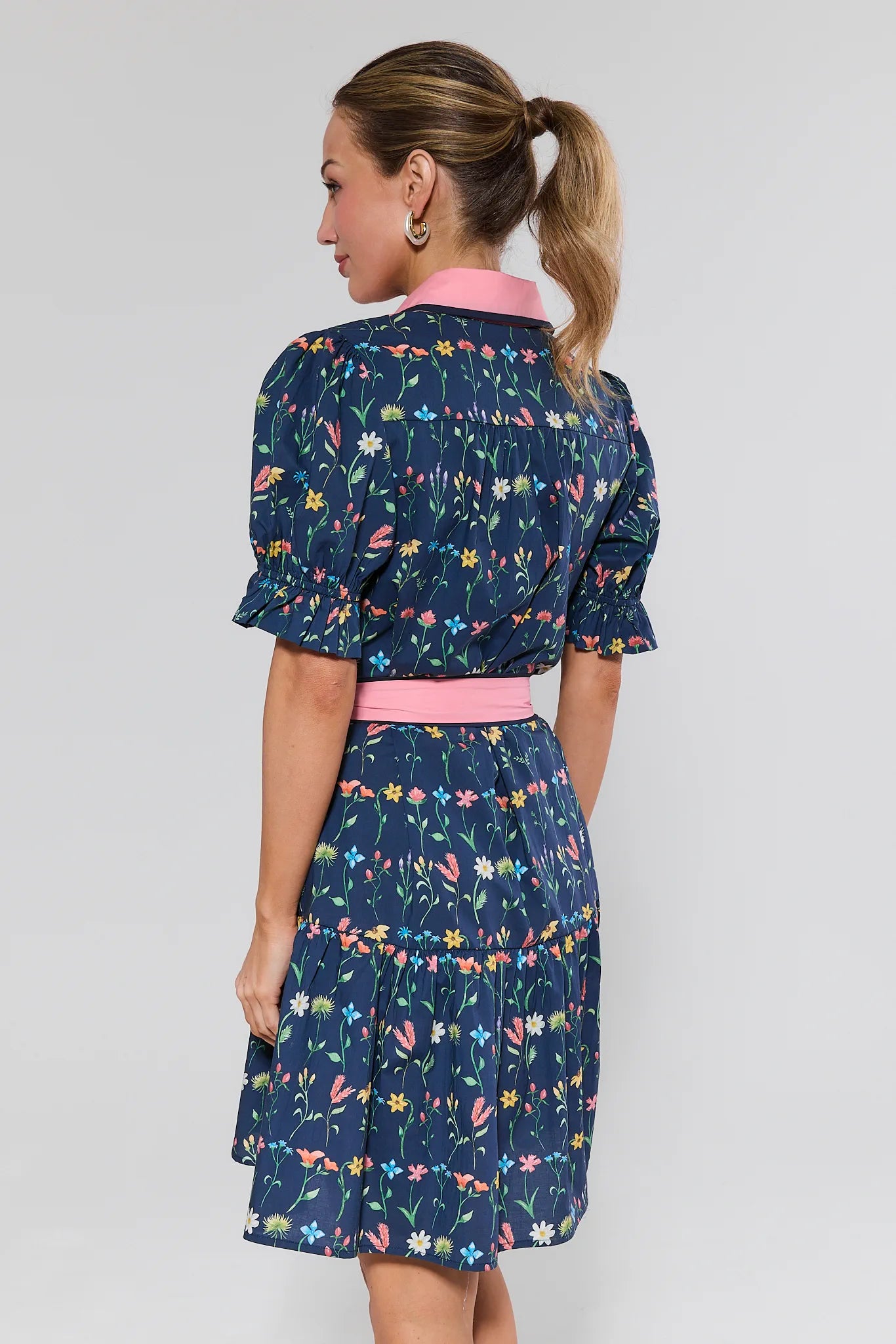 Woman wearing a navy floral dress with a pink belt on a plain background