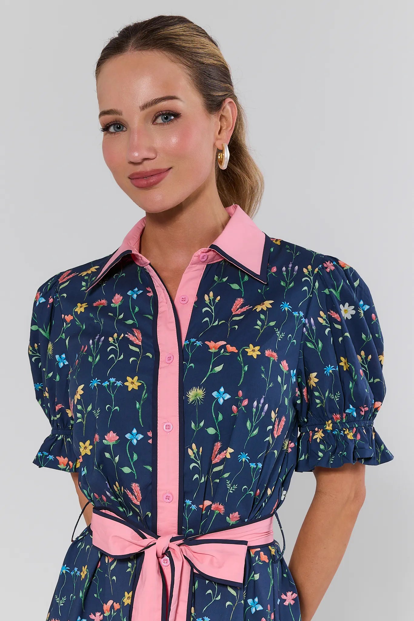 Woman wearing a navy dress with floral pattern and pink accents on a plain background