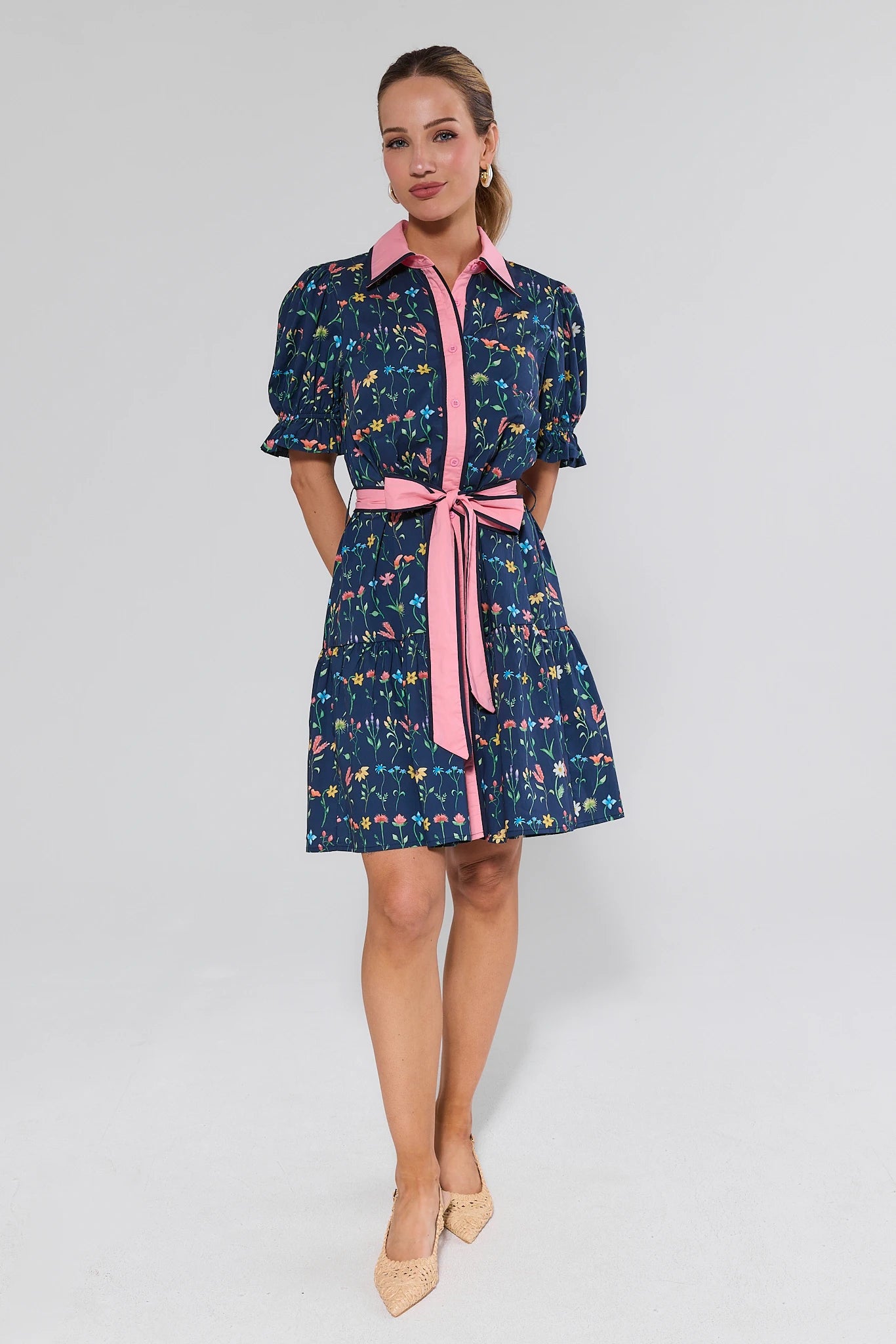 Woman wearing a patterned dress with a pink belt on a white background