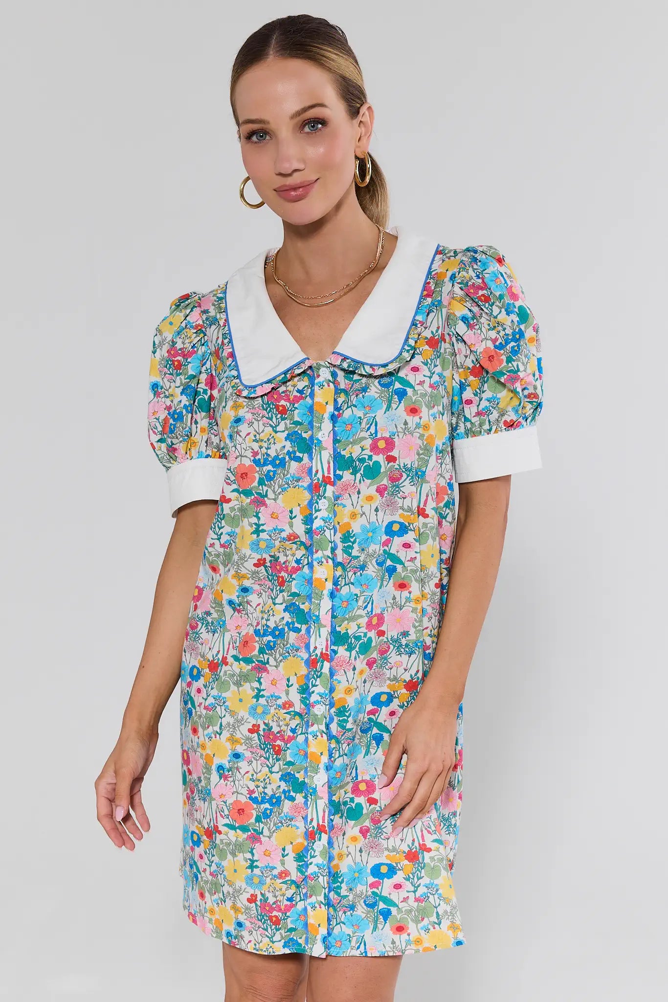 Woman wearing a colorful floral dress with a white collar on a plain background