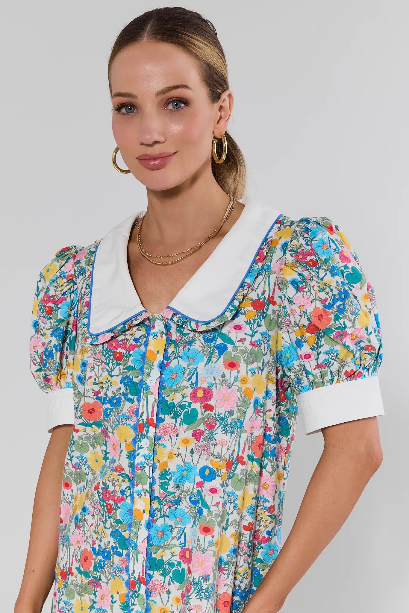 Woman wearing a colorful floral dress with a white collar on a plain background