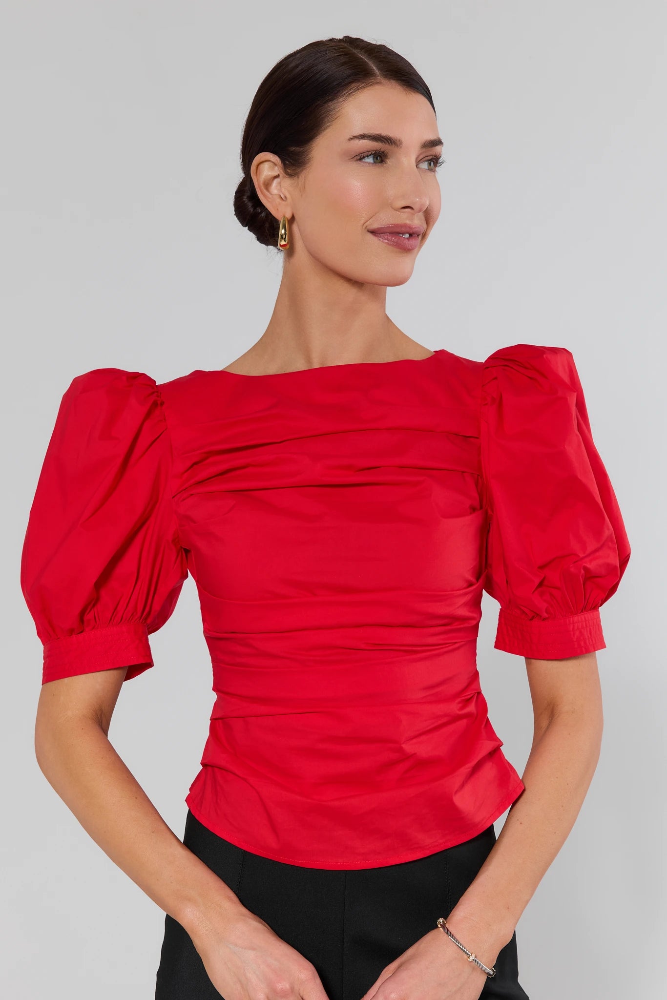 Woman wearing a red blouse with puffed sleeves against a gray background