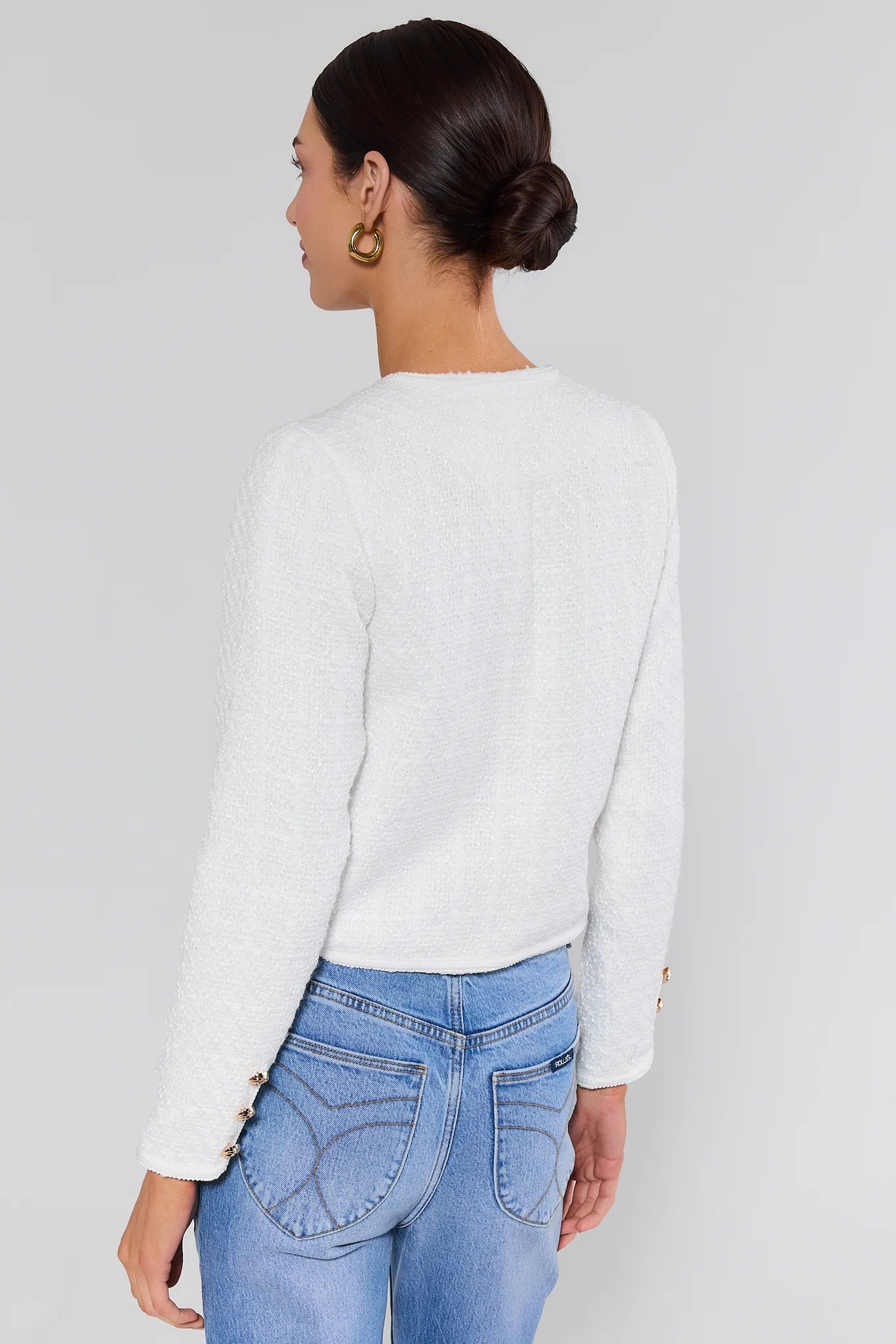 Woman standing wearing a white sweater and blue jeans on a plain background