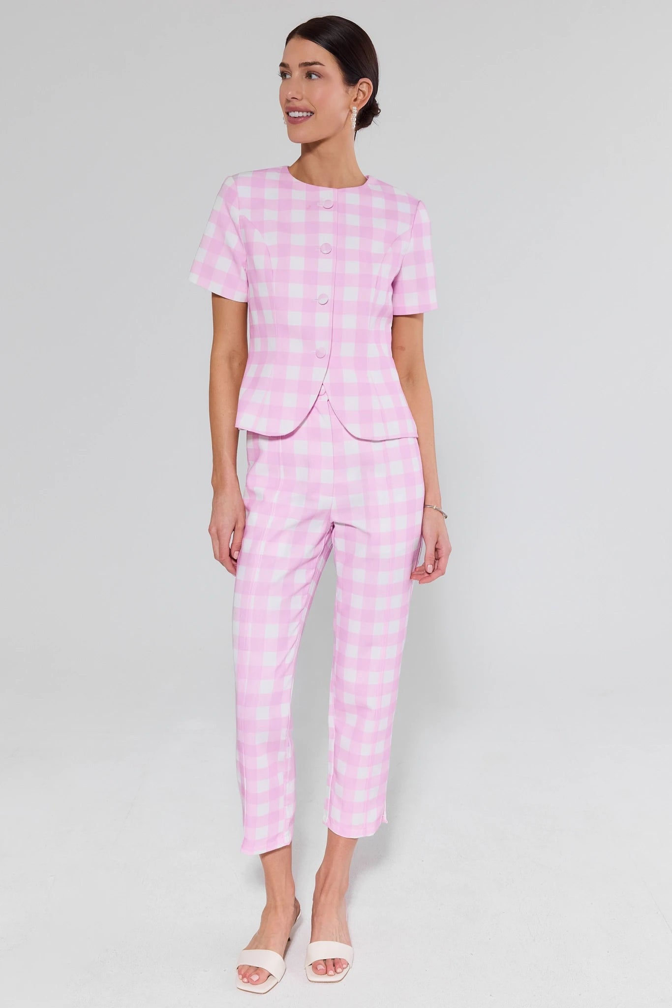Woman wearing a pink checkered outfit and white heels on a white background