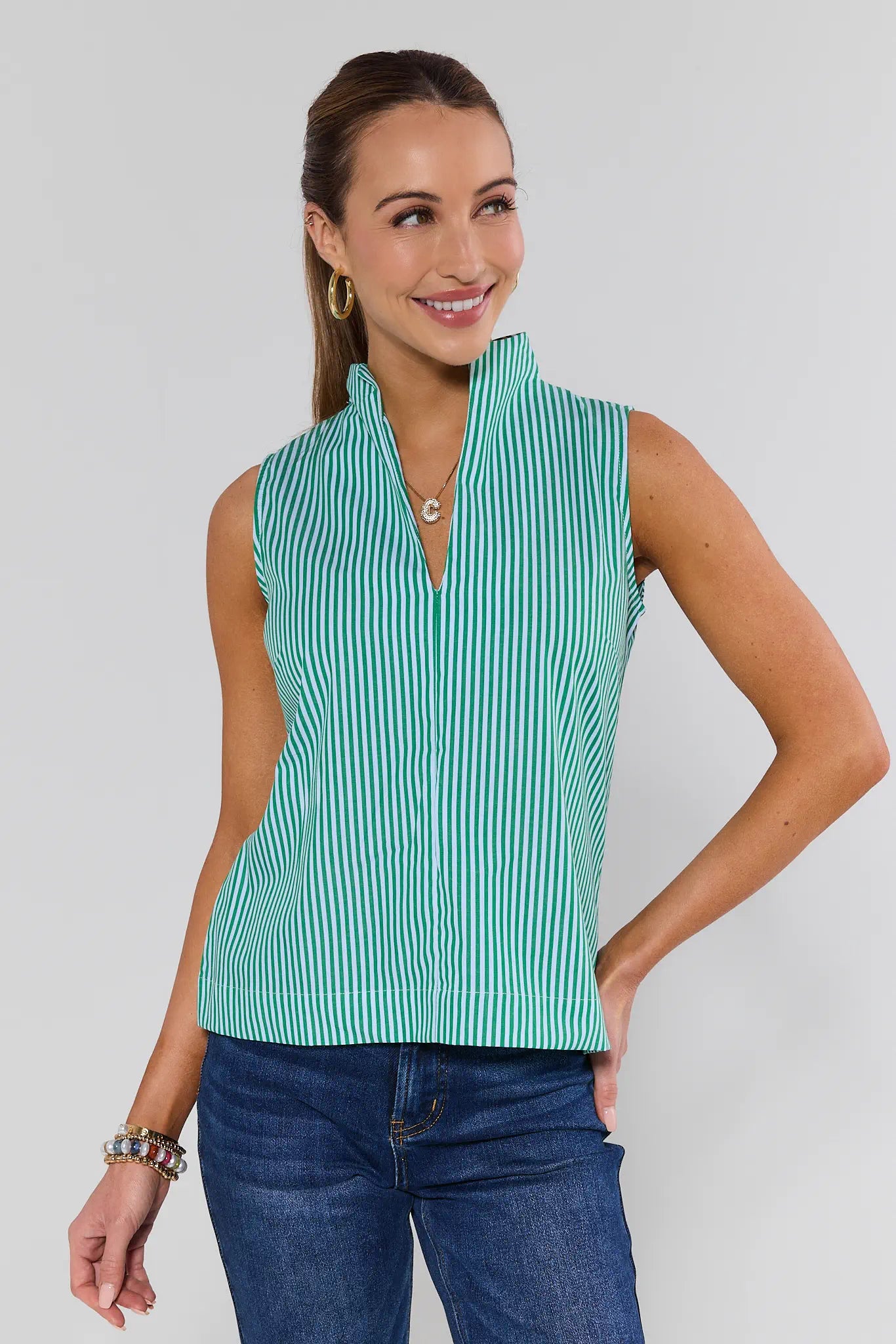 Woman wearing a green and white striped sleeveless top with blue jeans on a plain background