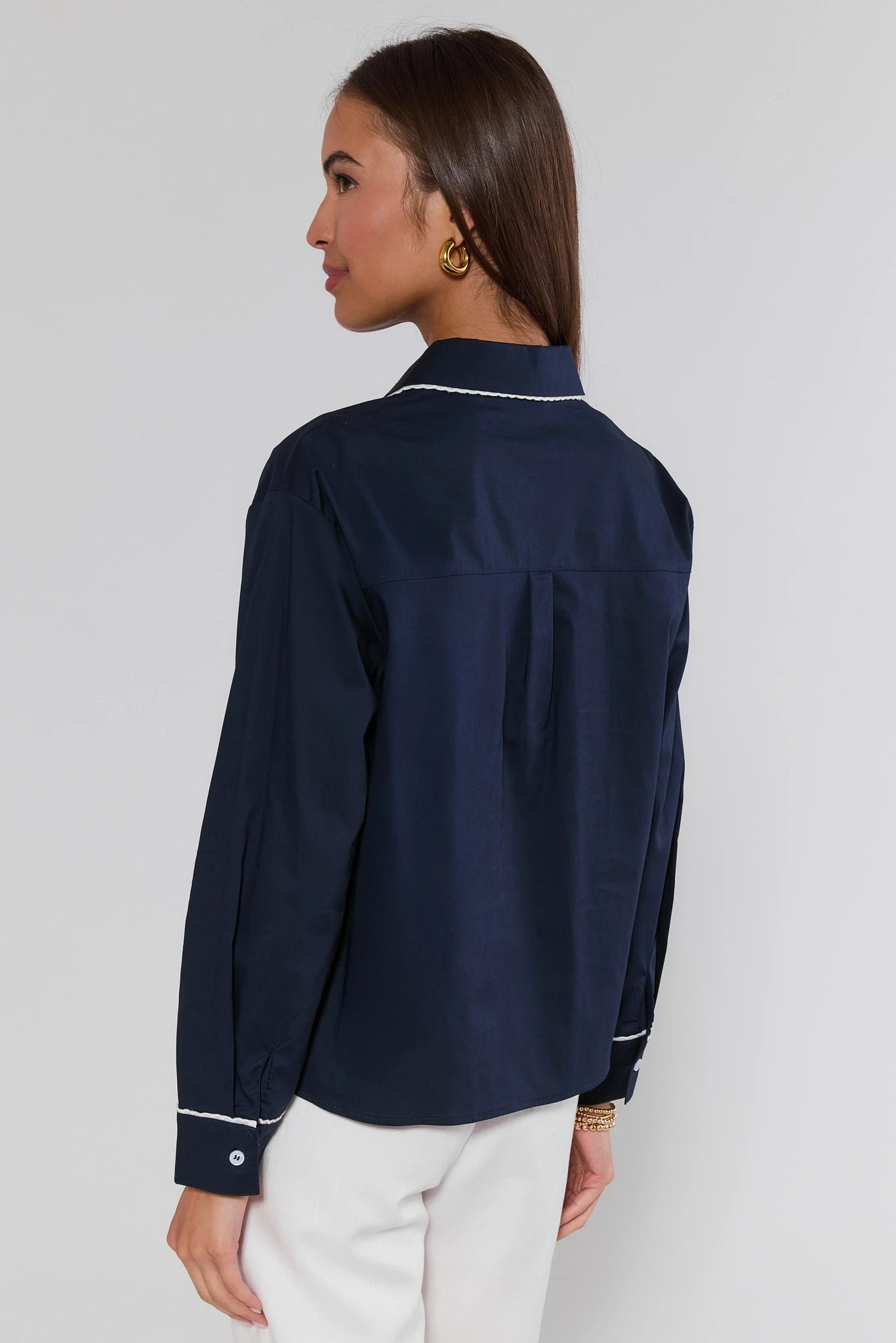 Woman wearing a navy blue satin shirt with white trim on a plain background