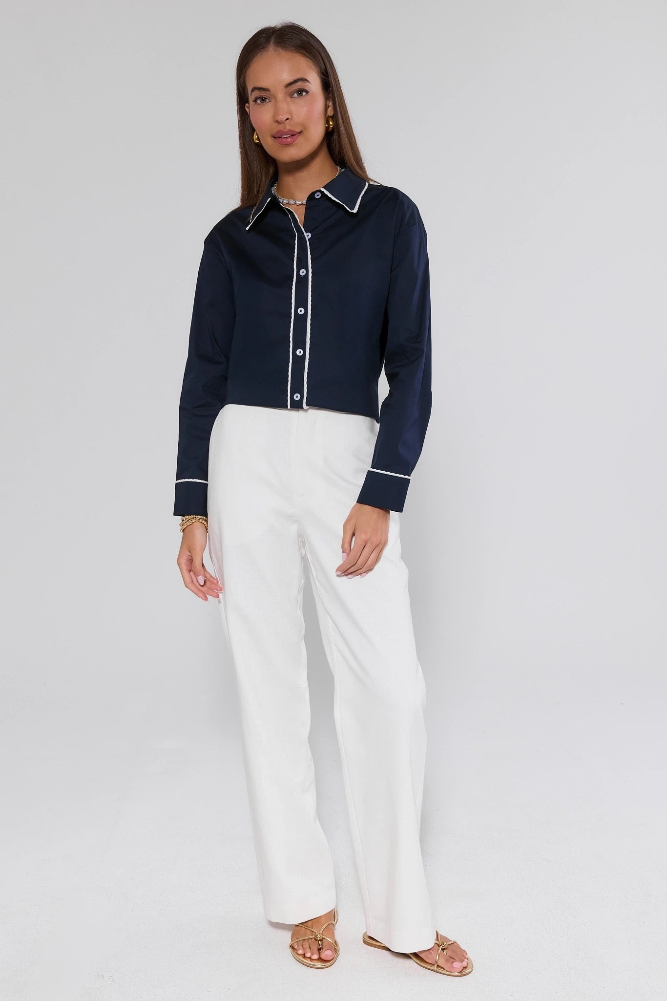 Woman wearing a navy blue shirt with white trim and white pants on a plain background
