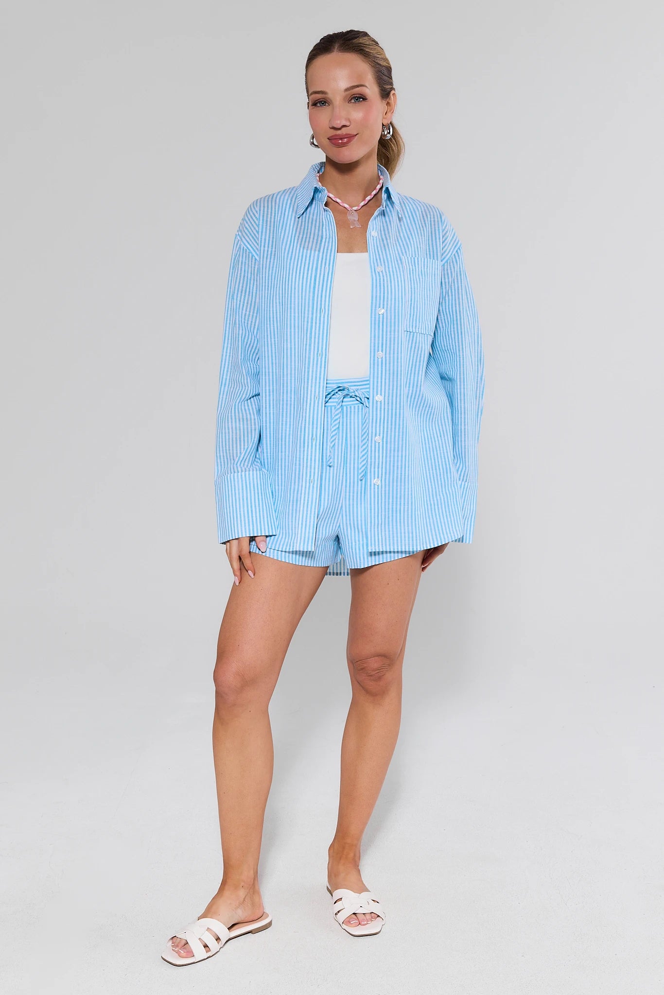 Woman wearing a light blue striped shirt and shorts set on a gray background