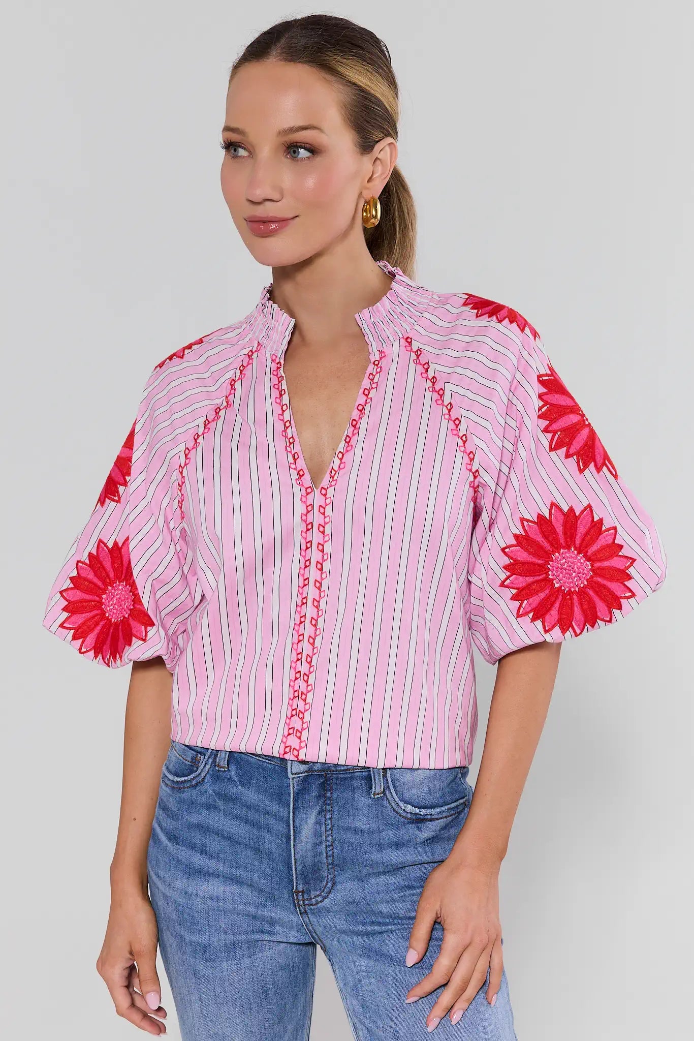 Woman wearing a pink and white striped blouse with red floral accents on a plain background