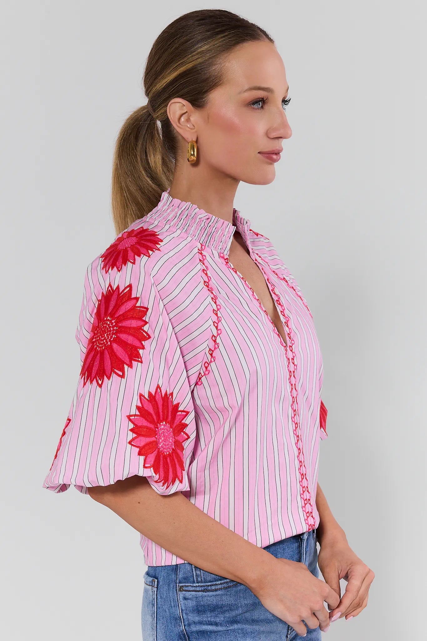 Woman wearing a pink striped blouse with red floral patterns on a gray background