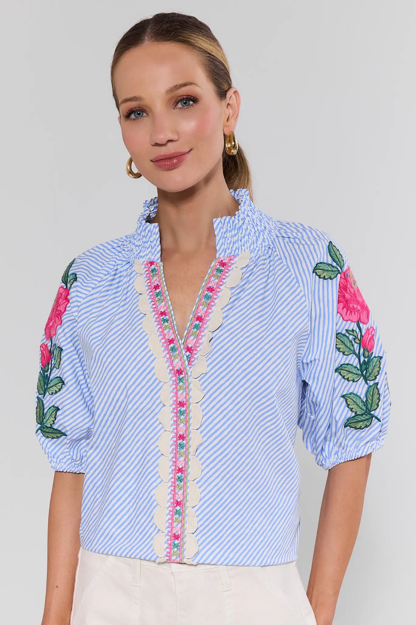 Woman wearing a blue embroidered blouse with floral designs on a white background