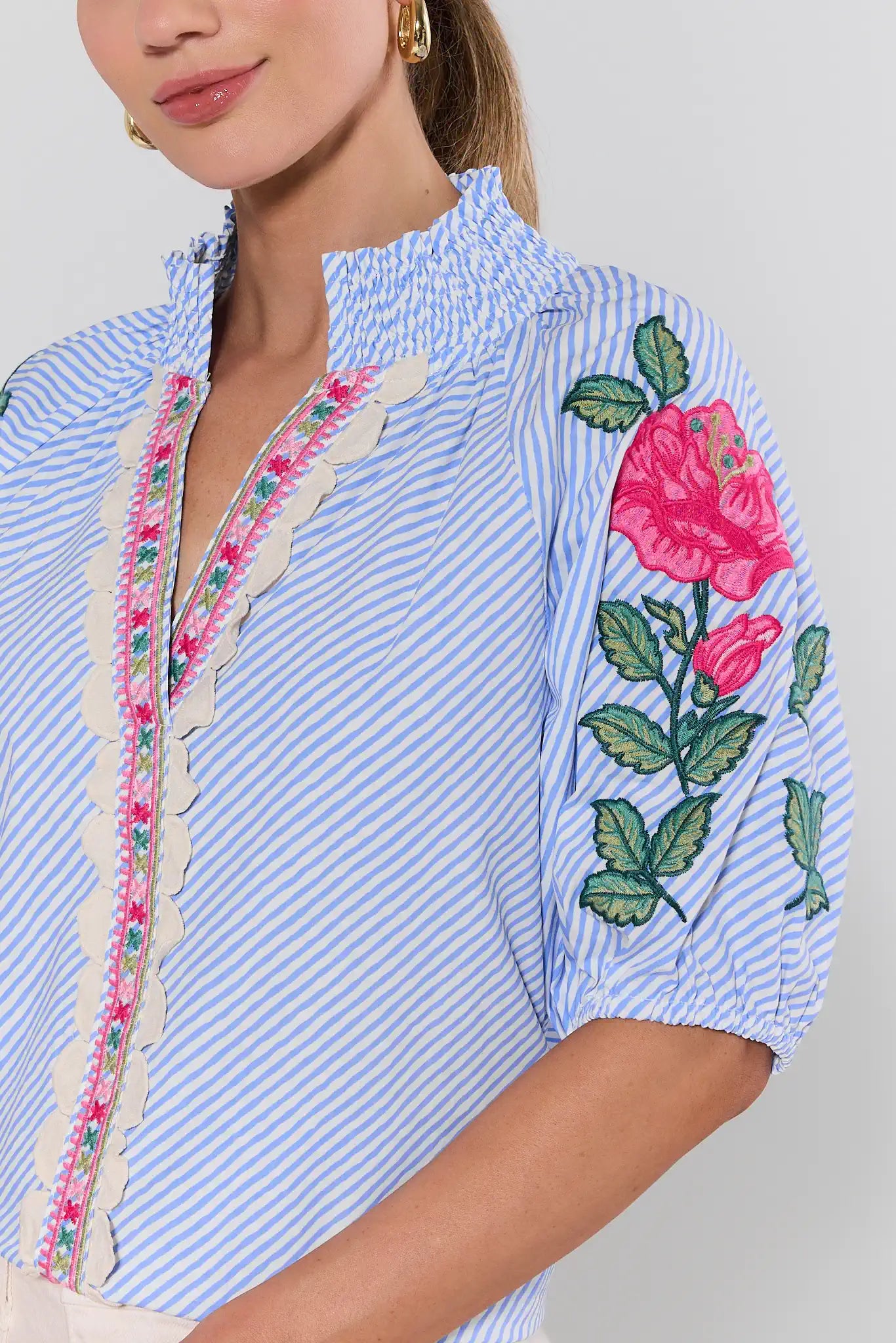 Close-up of a blue and white striped blouse with floral embroidery on a plain background