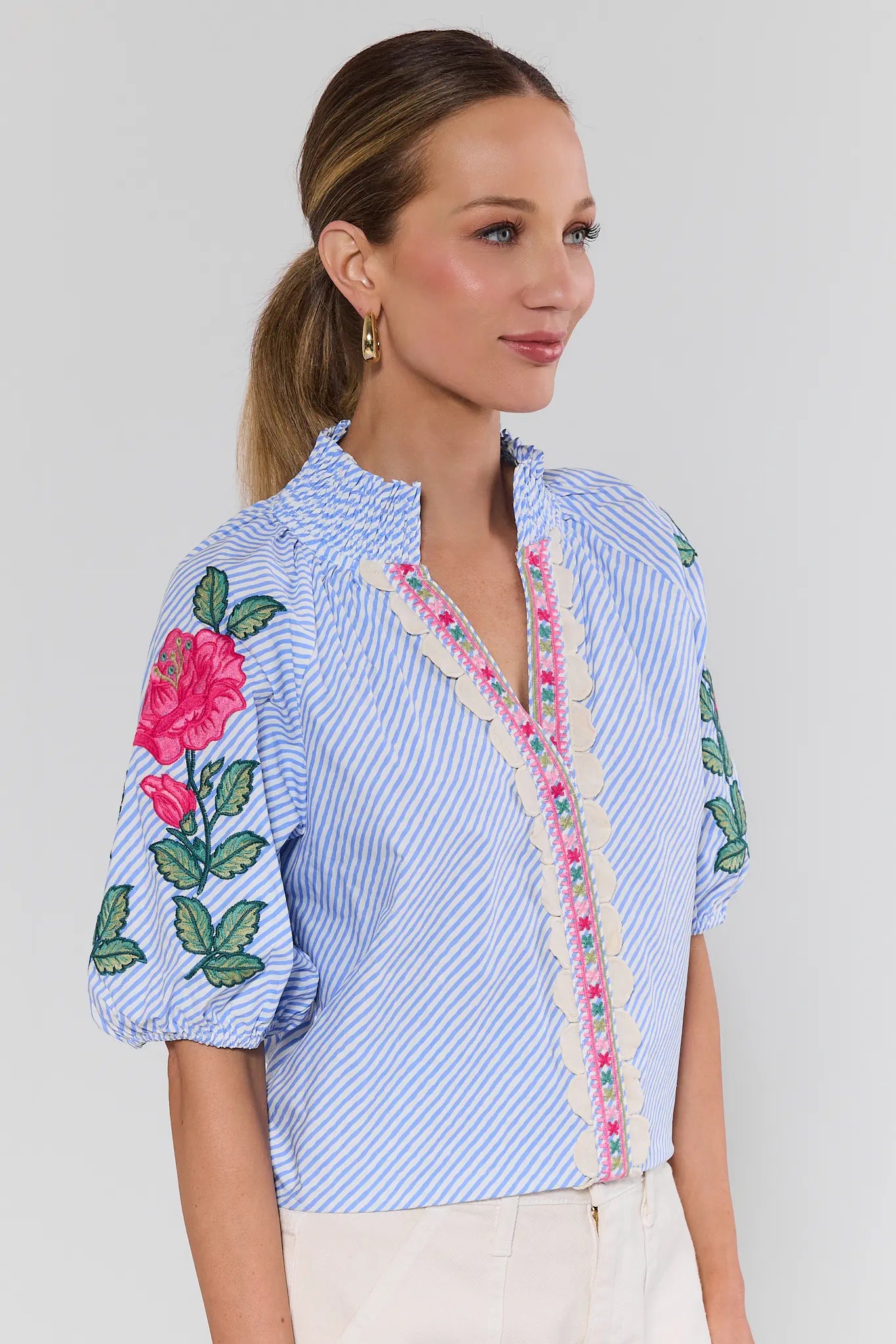 Woman wearing a blue striped shirt with floral embroidery on a background