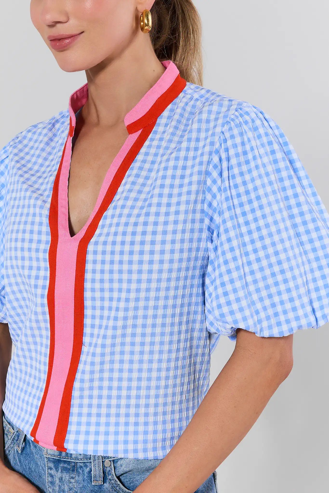 Woman wearing a blue and white checkered shirt with pink and red accents on a gray background