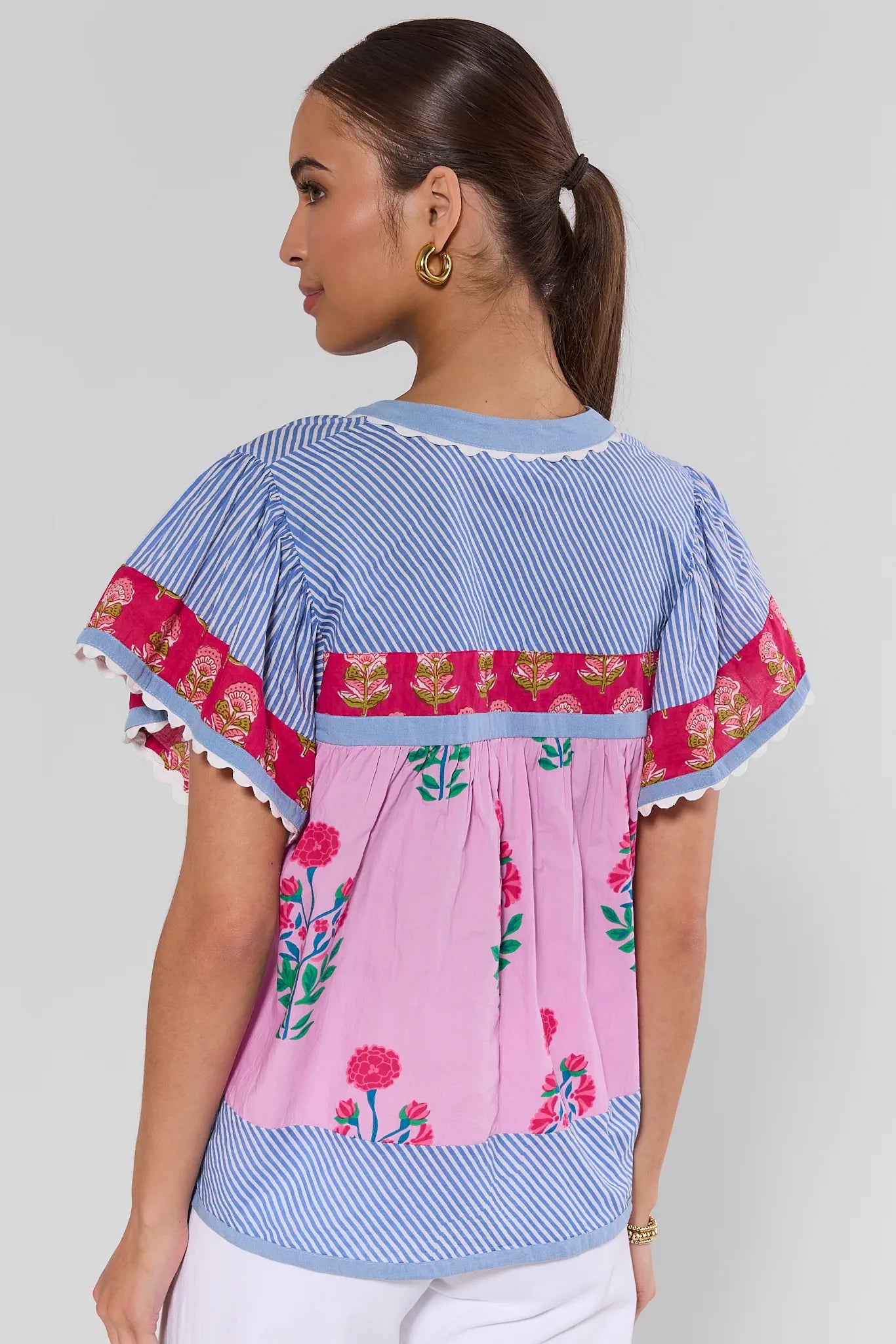Woman wearing a colorful blouse with floral and striped patterns on a plain background