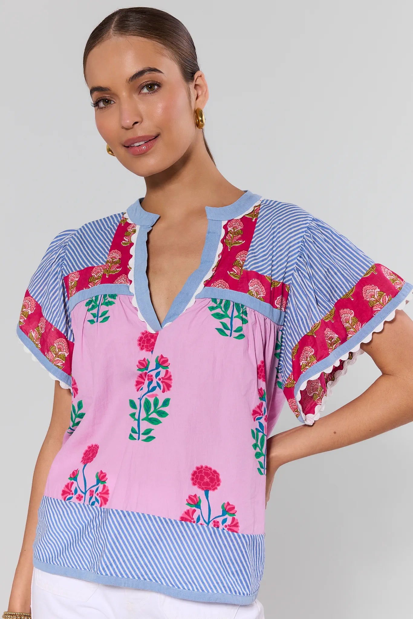Woman wearing a pink and blue embroidered top with floral patterns on a plain background