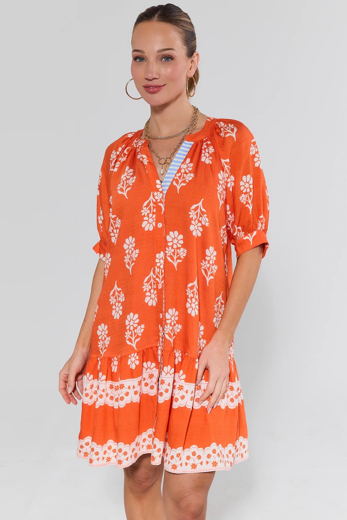 Woman wearing an orange floral dress a plain background