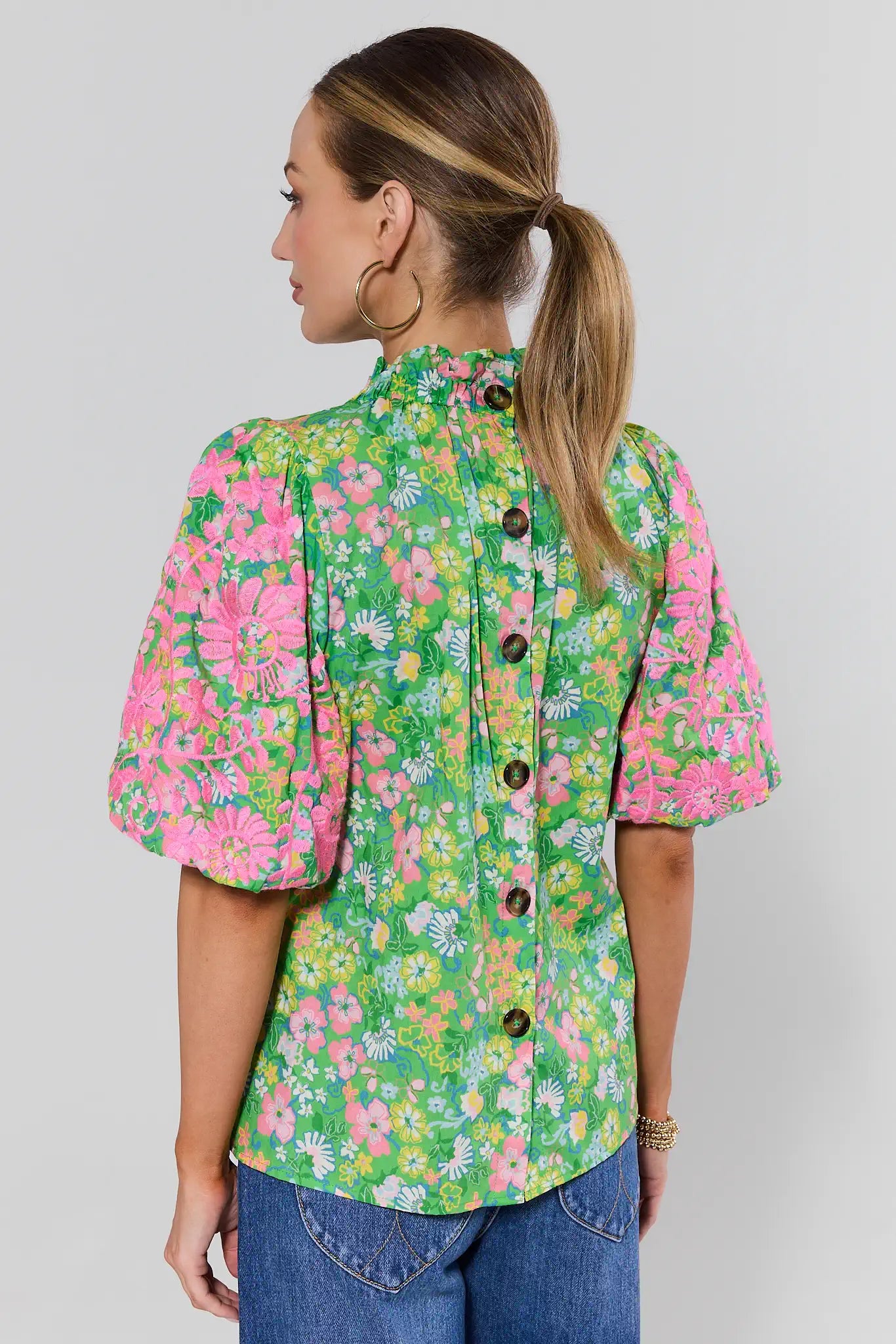 Woman standing wearing a floral blouse with a plain background
