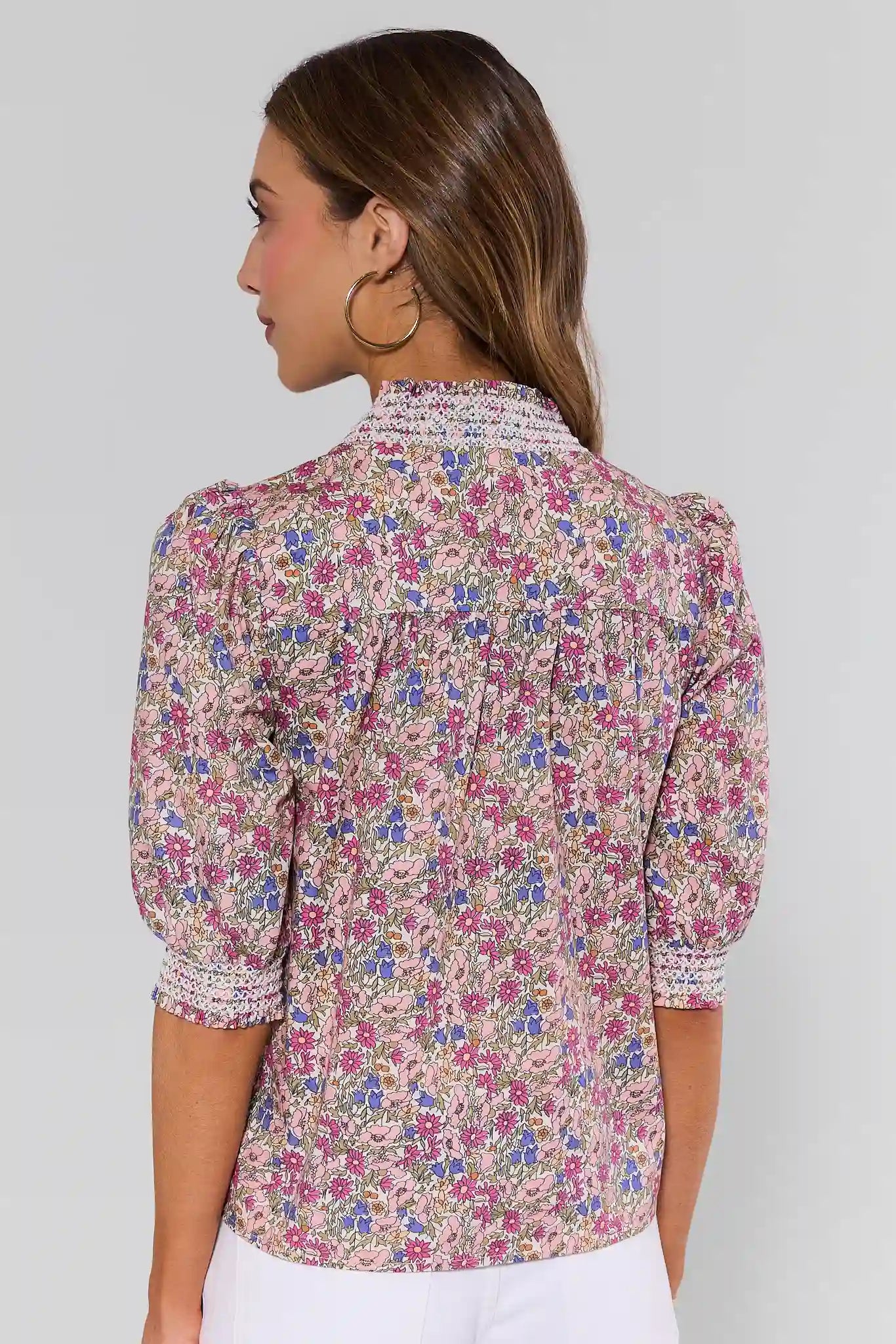 Woman standing wearing a floral blouse against a plain background