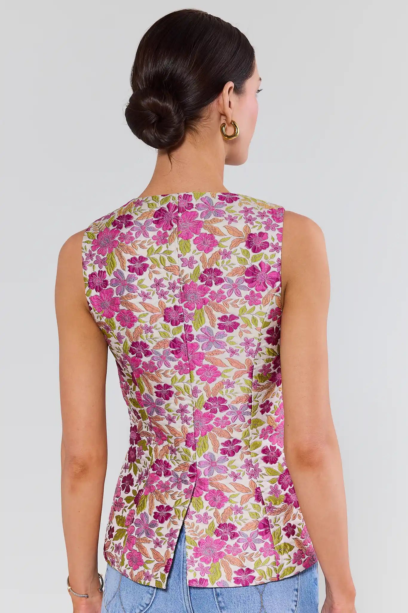 Woman standing wearing a sleeveless floral top with a plain background