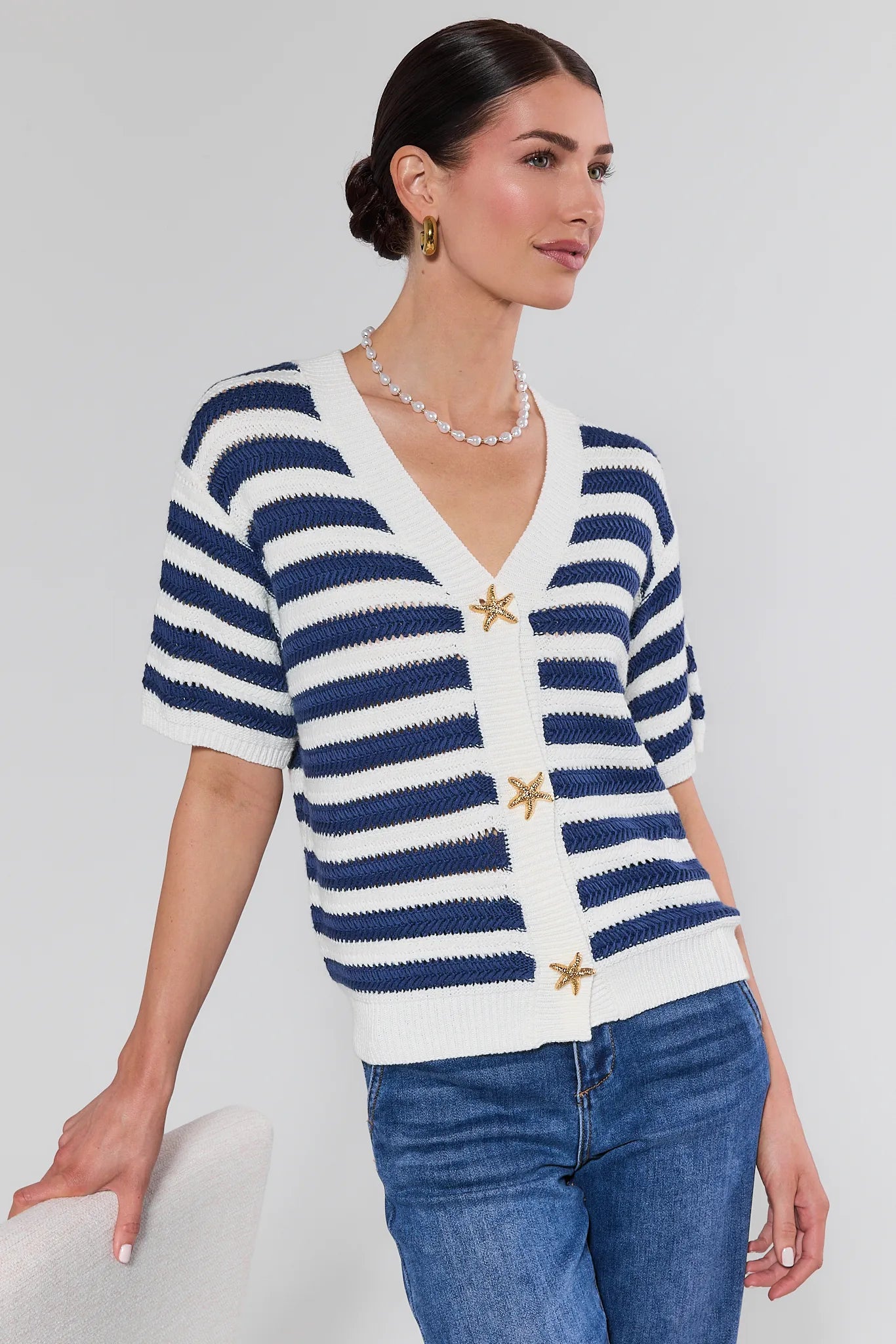 Woman wearing a blue and white striped cardigan with star details on a plain background
