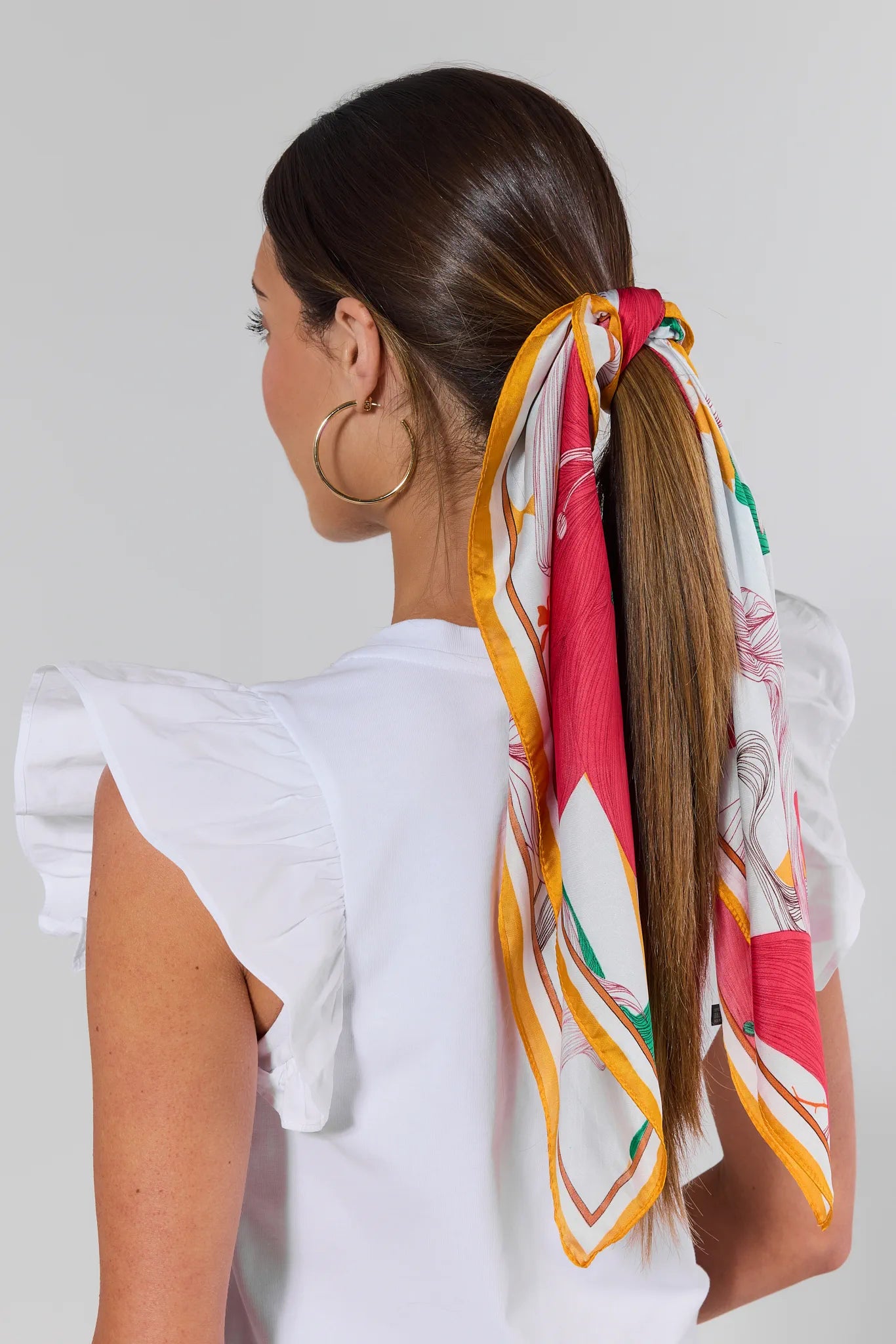 Woman with a colorful scarf tied in her hair against a plain background
