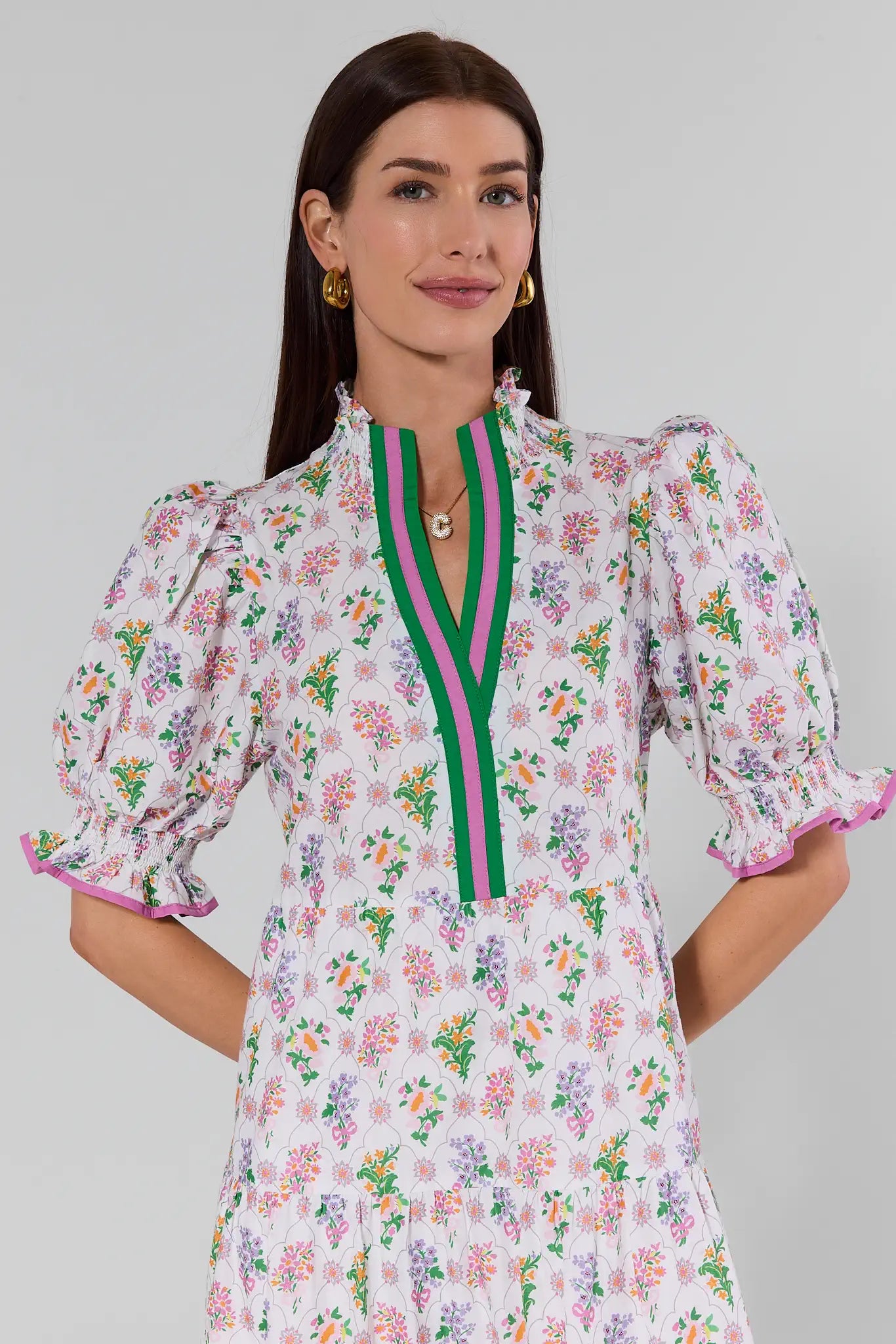 Woman wearing a floral dress with a green and pink trim on a gray background