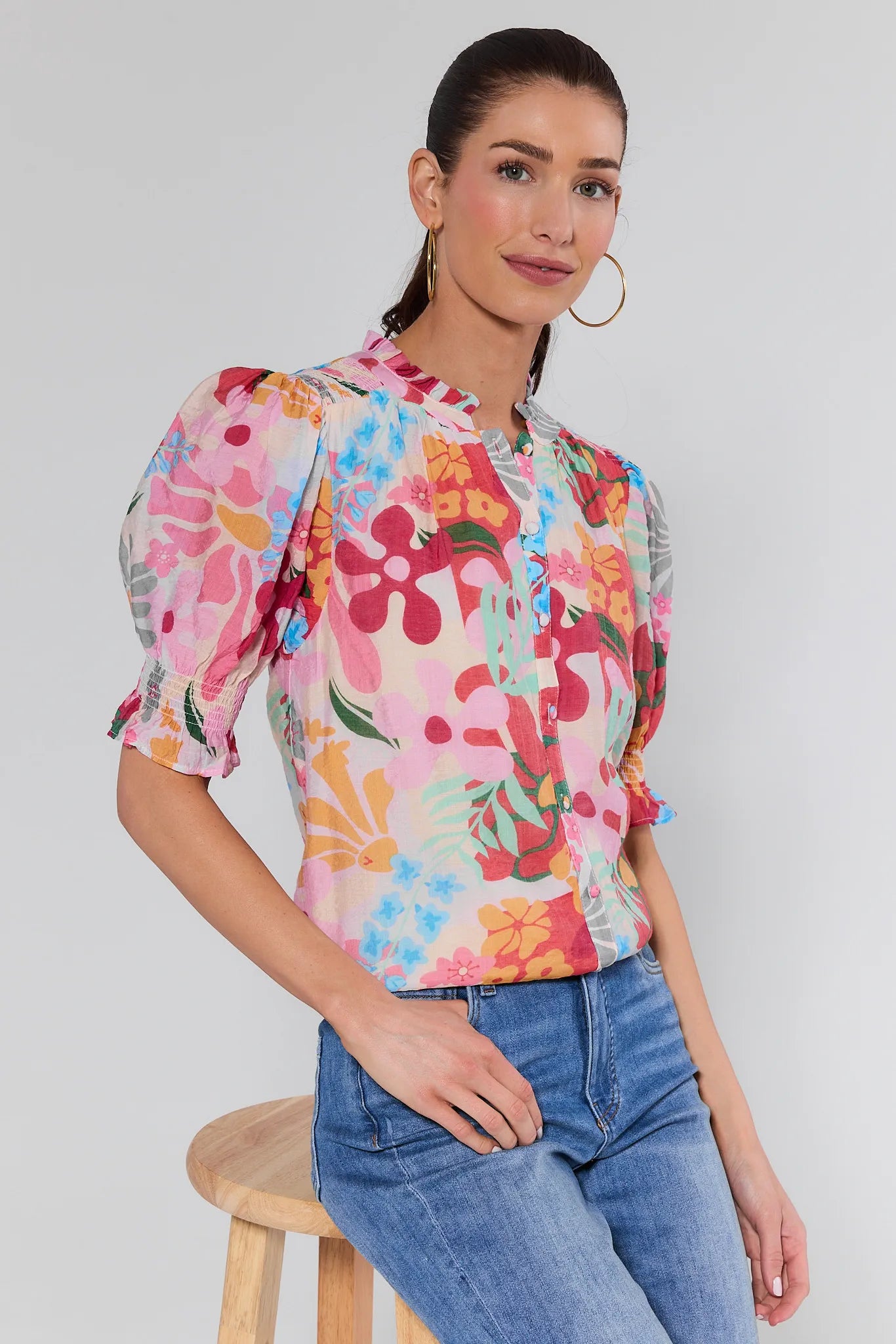 Woman wearing a colorful floral blouse and blue jeans against a white background