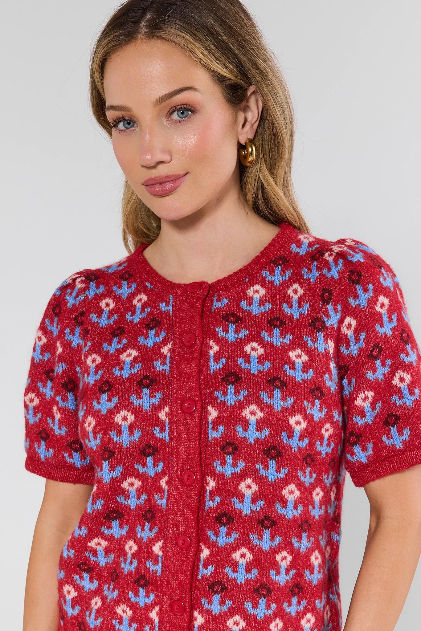 Woman wearing a red knitted cardigan with floral pattern on a plain background