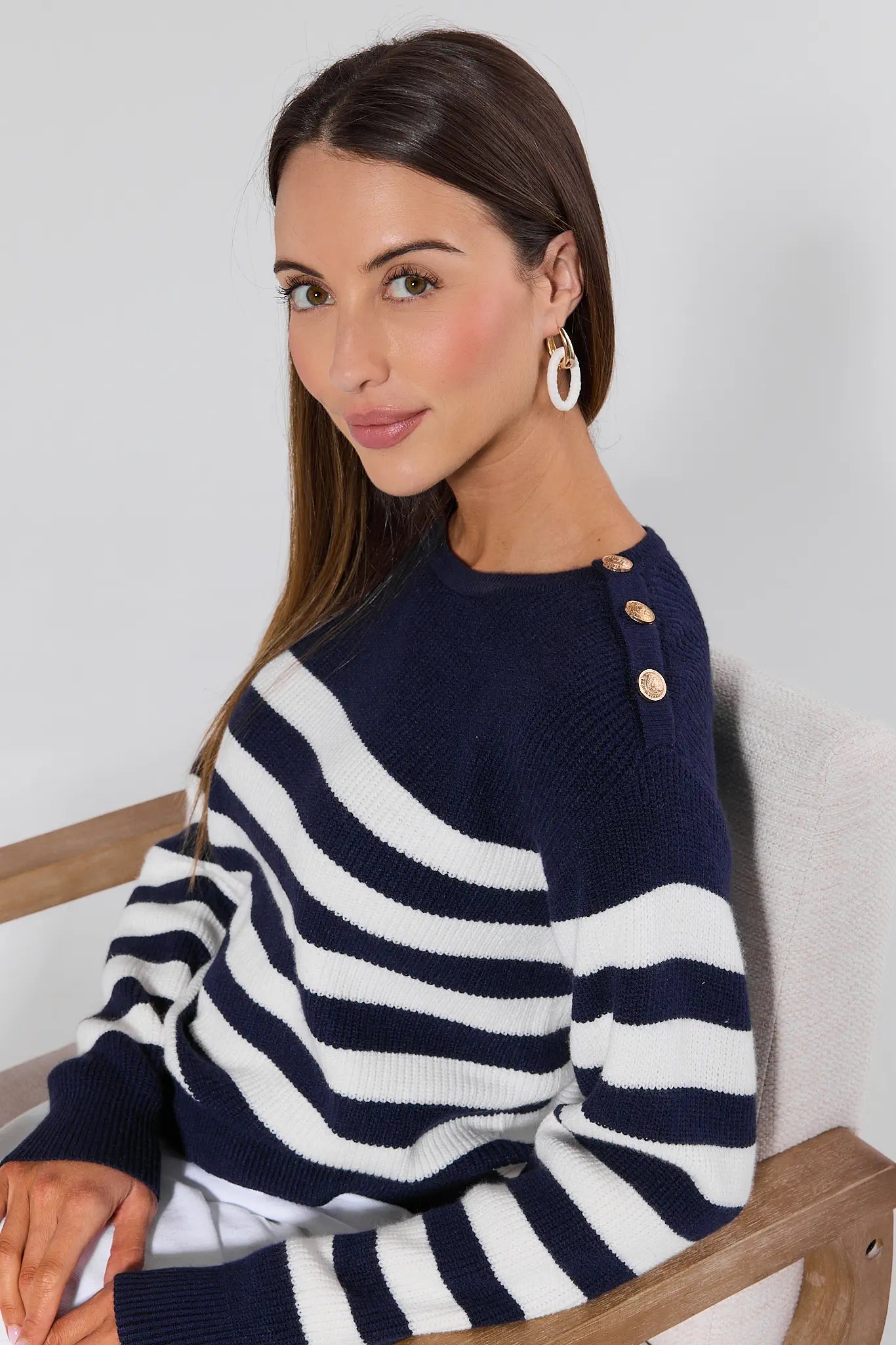 Woman wearing a navy and white striped sweater with gold buttons, sitting on a wooden chair.